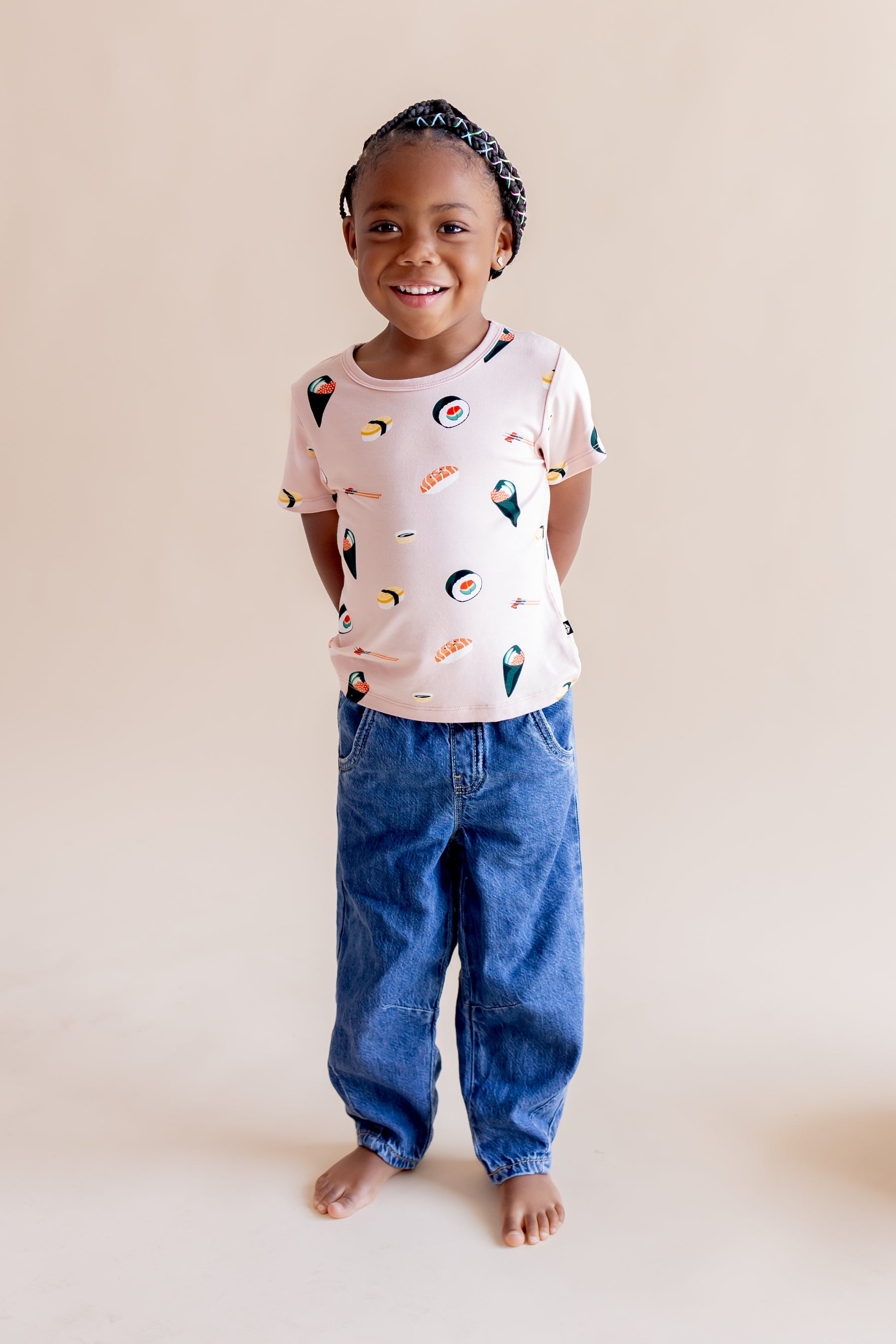 Child standing and smiling wearing blush sushi tee with jeans