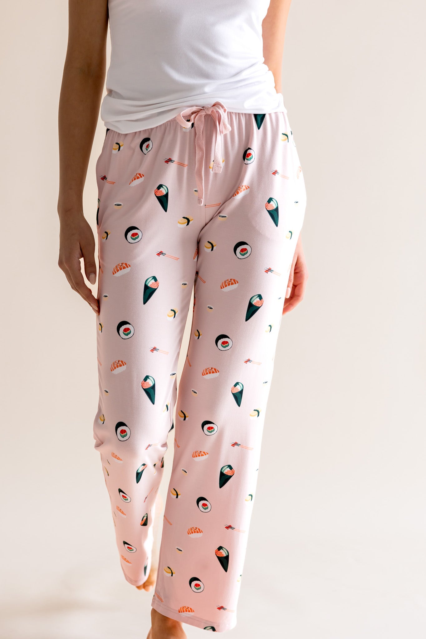 Model wearing pink Women's Lounge Pants with drawstring in Sushi print under white camisole on a beige background