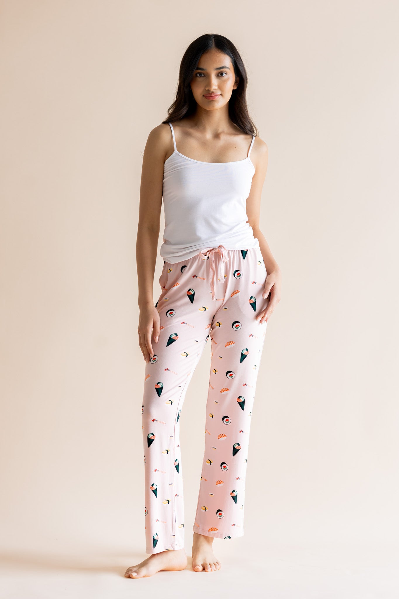 Model posing in pink Women's Lounge Pants in Sushi print under white camisole on a beige background