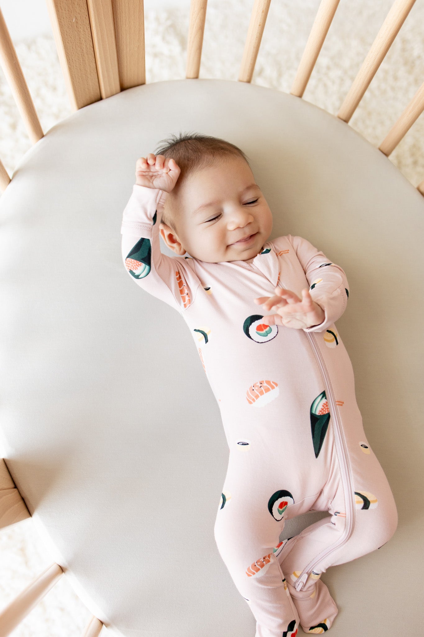 Baby sleeping in crib wearing Zippered Footie in Blush Sushi print