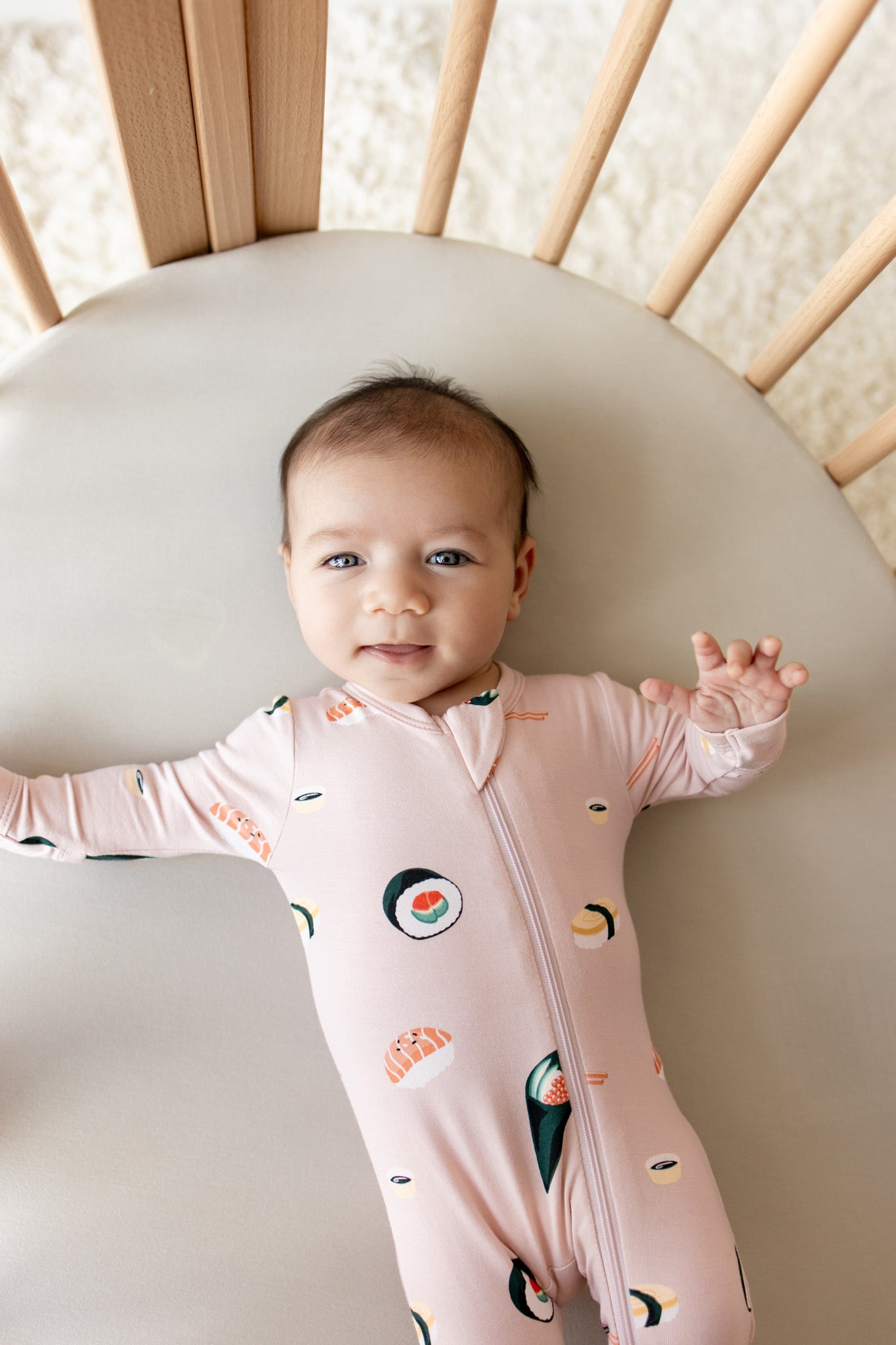 Baby lying in crib wearing pink Zippered Footie in Sushi print