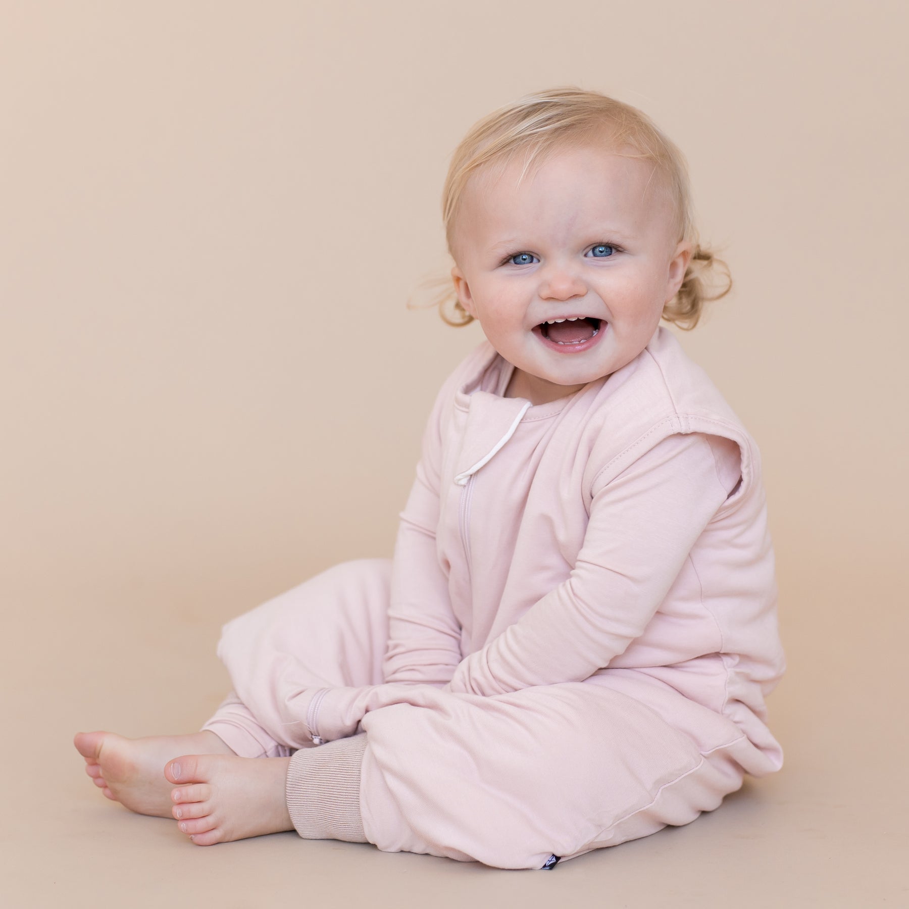 Young toddler sitting wearing a blush pink sleep bag walker and matching pajamas