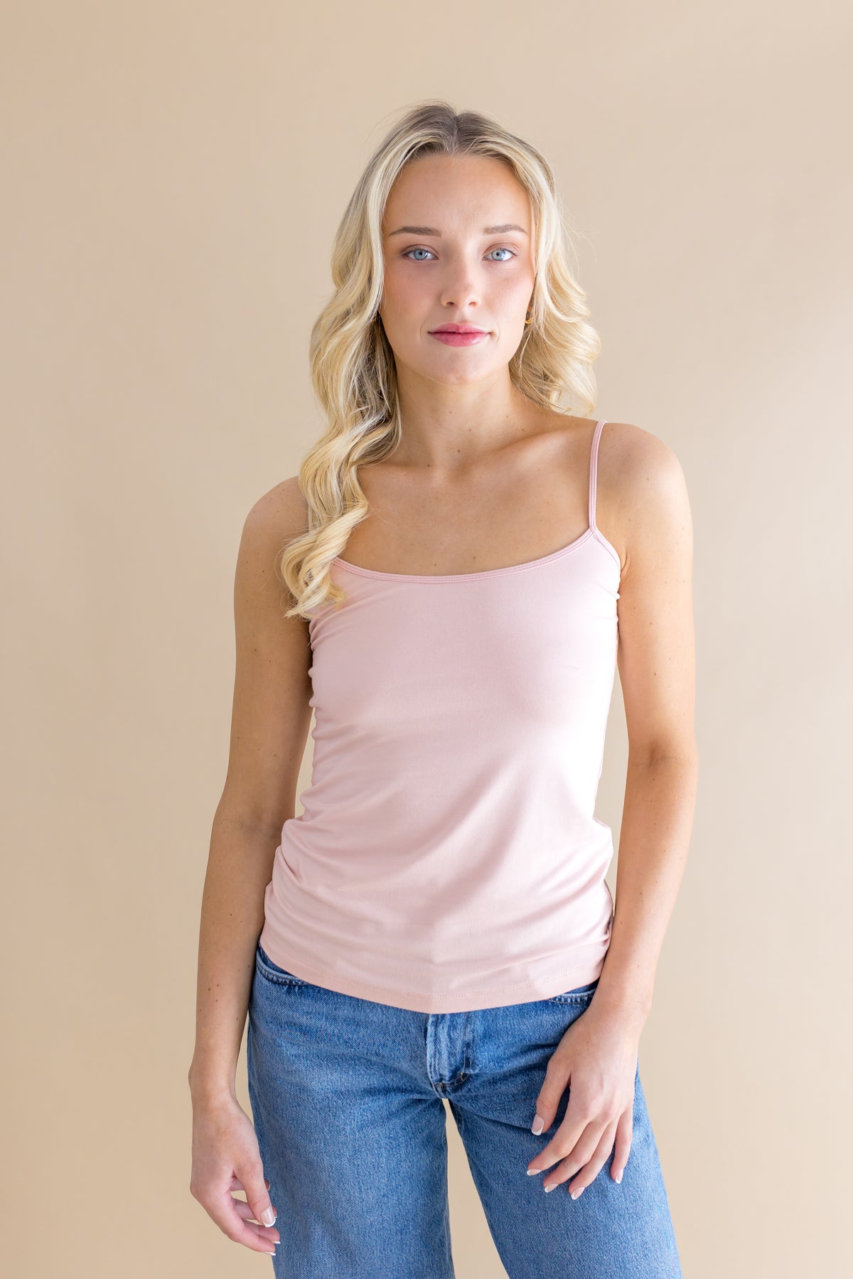 Woman wearing a light pink tank top and blue jeans against a beige background