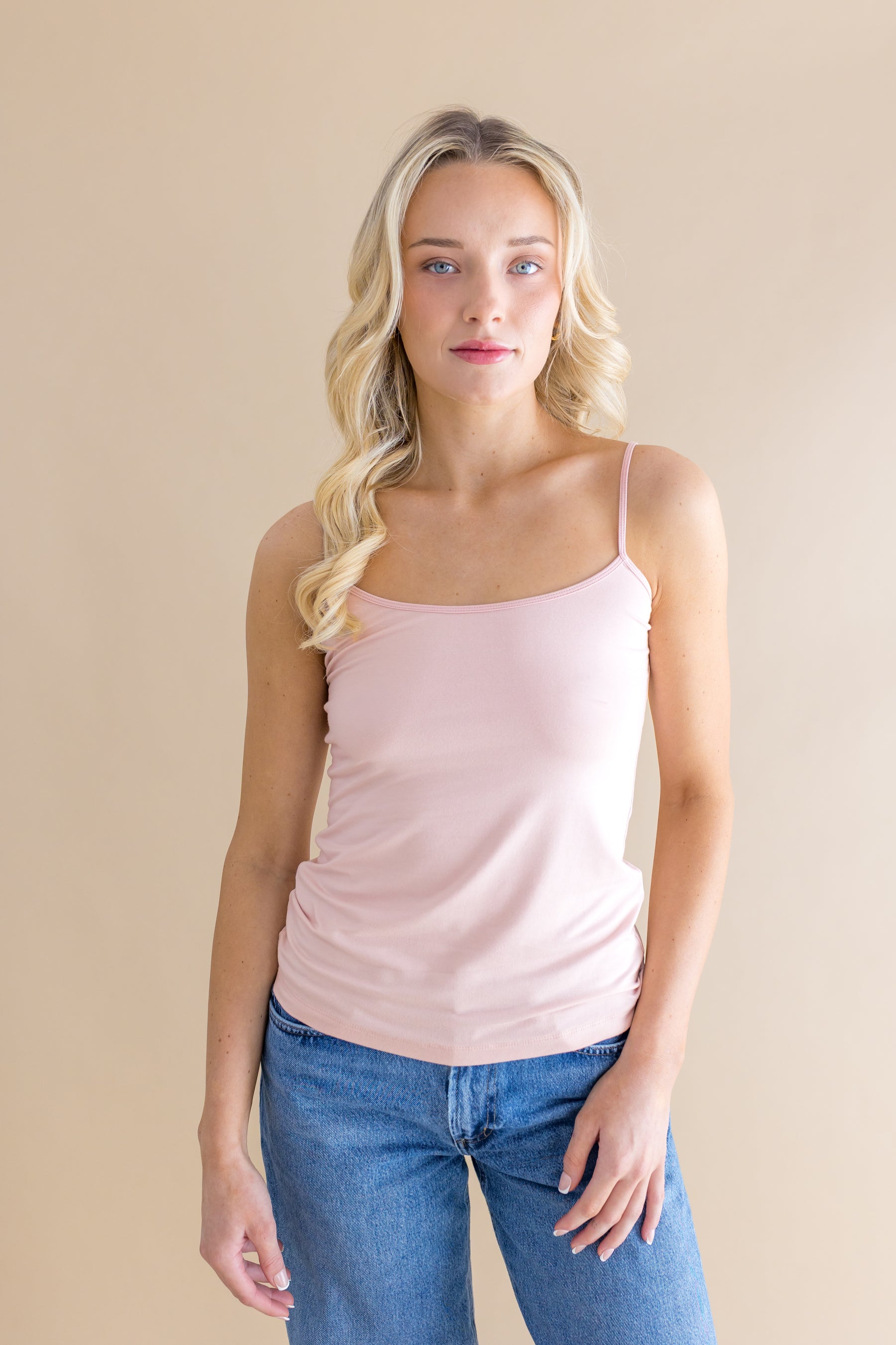 Woman wearing a light pink tank top and blue jeans against a beige background