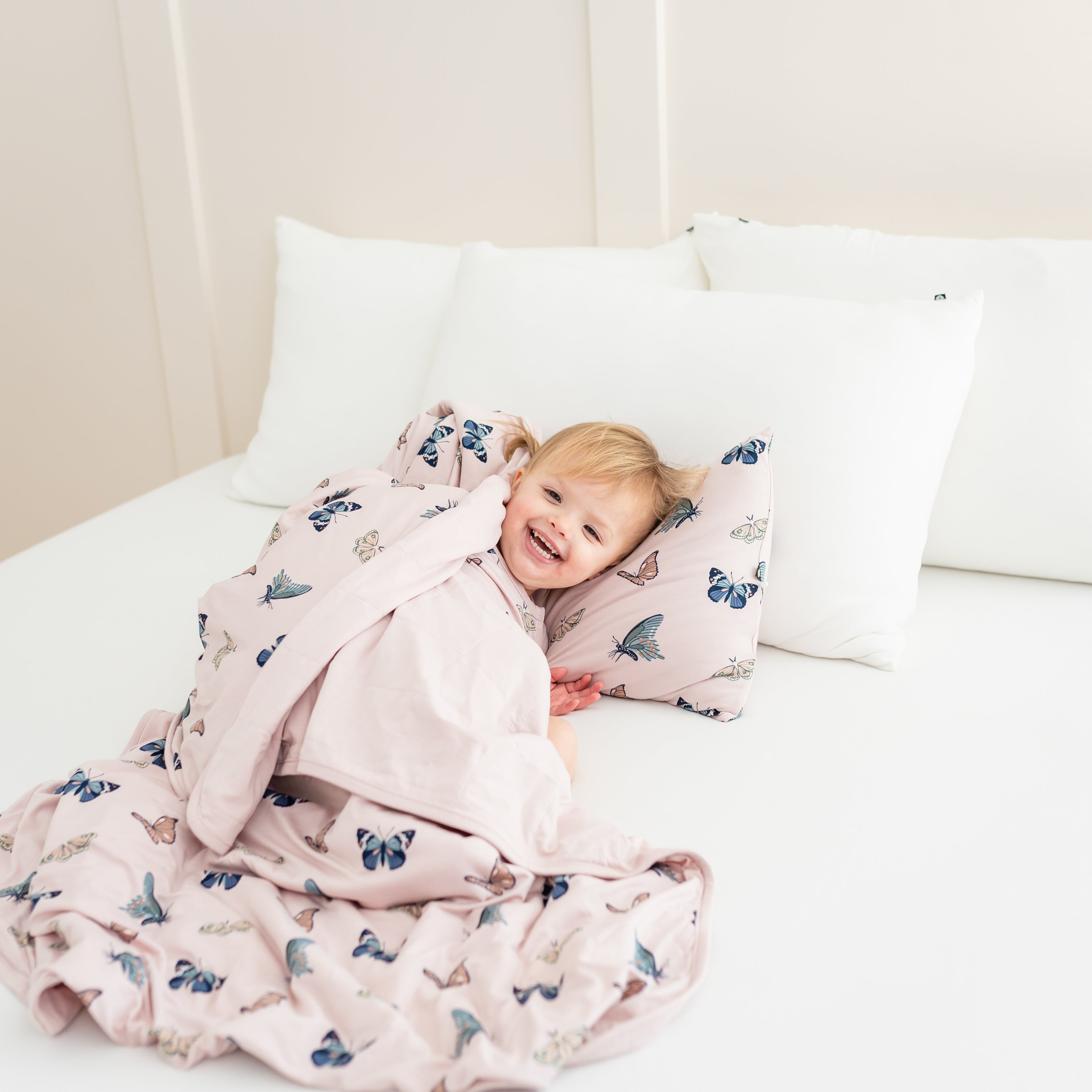 Toddler snuggled in 1.0 toddler blanket in blush butterfly and matching pillow