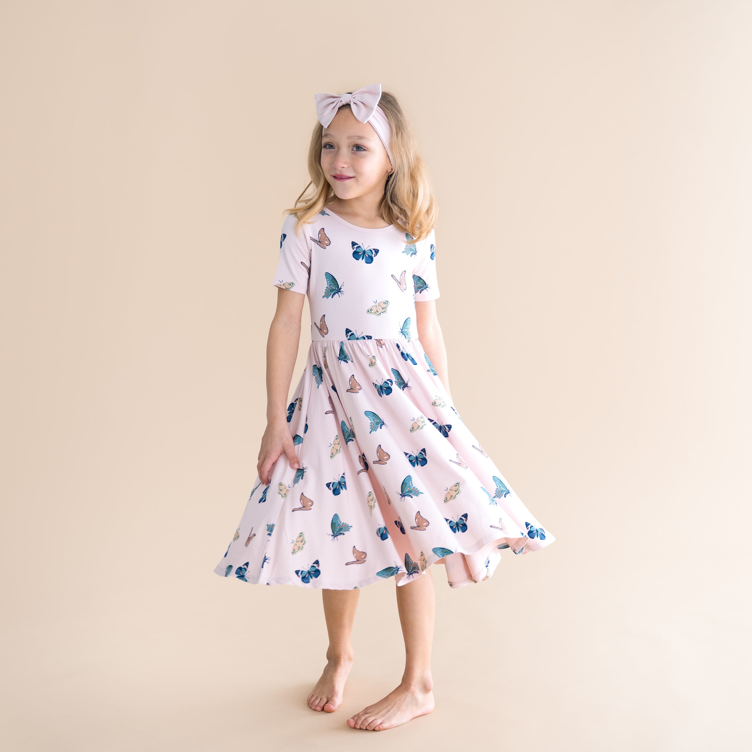 Young girl wearing a butterfly-patterned dress against a beige background