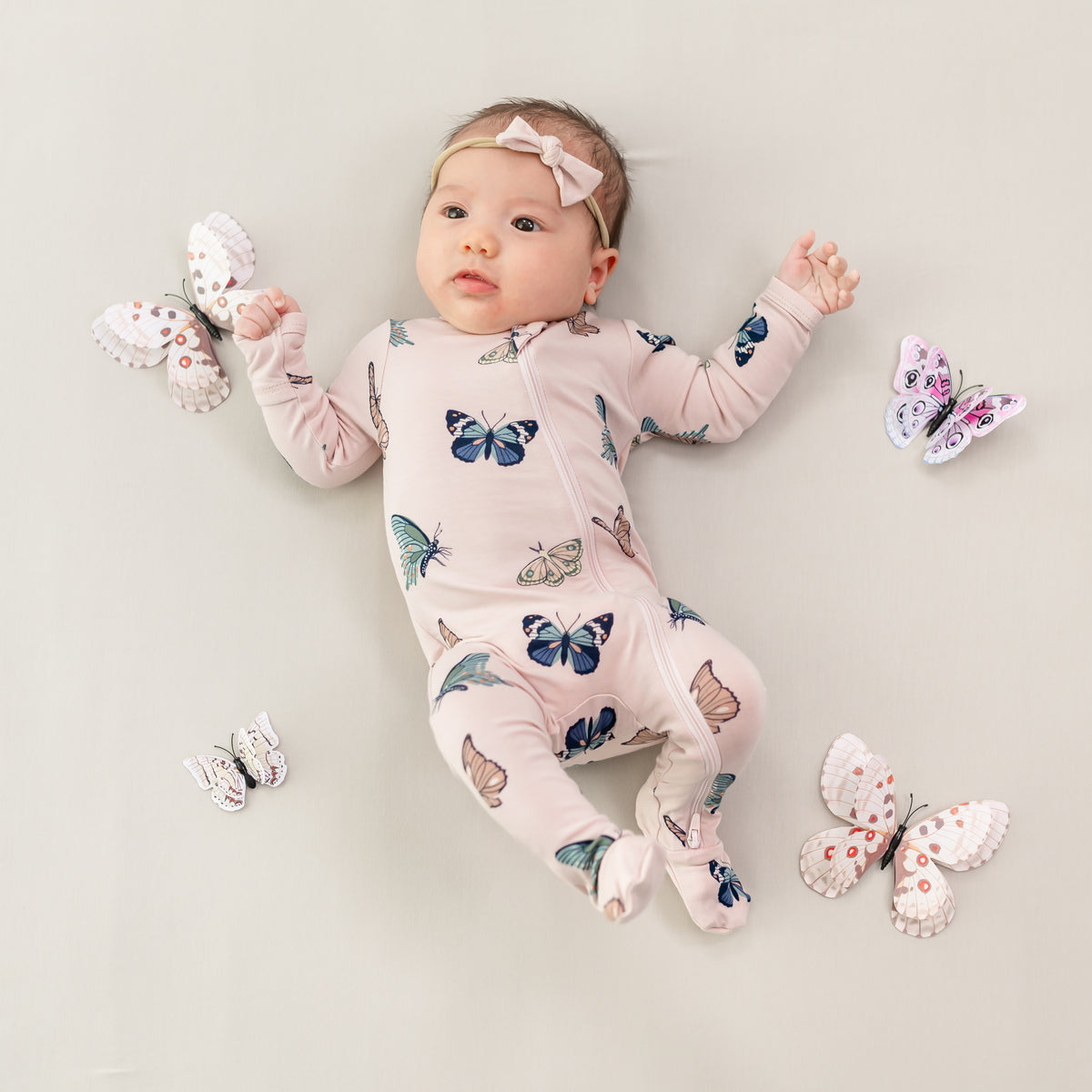 Baby wearing Zippered Footie in Blush Butterfly surrounded by butterfly props