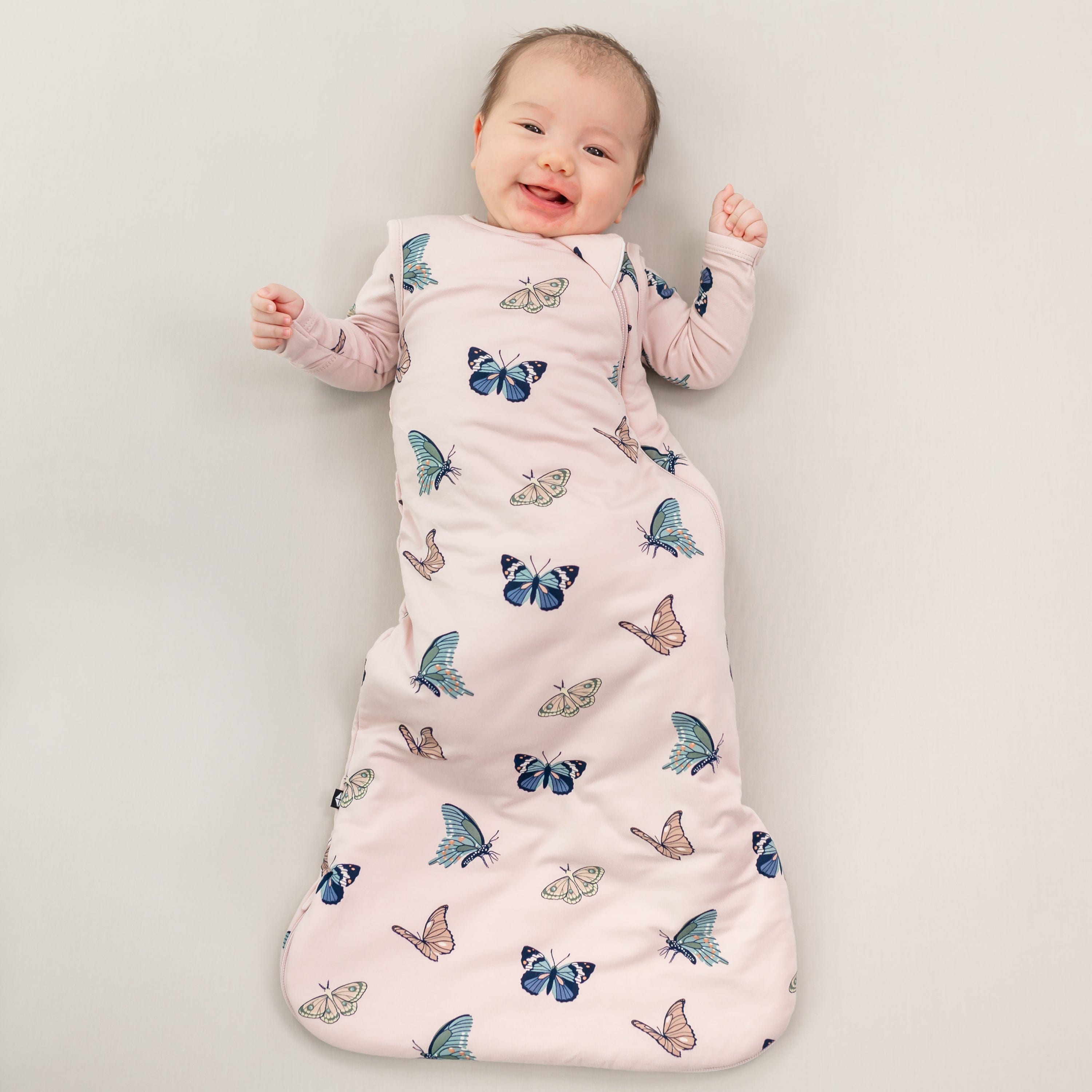 Baby smiling wearing 1.0 Sleep Bag in Blush Butterfly 