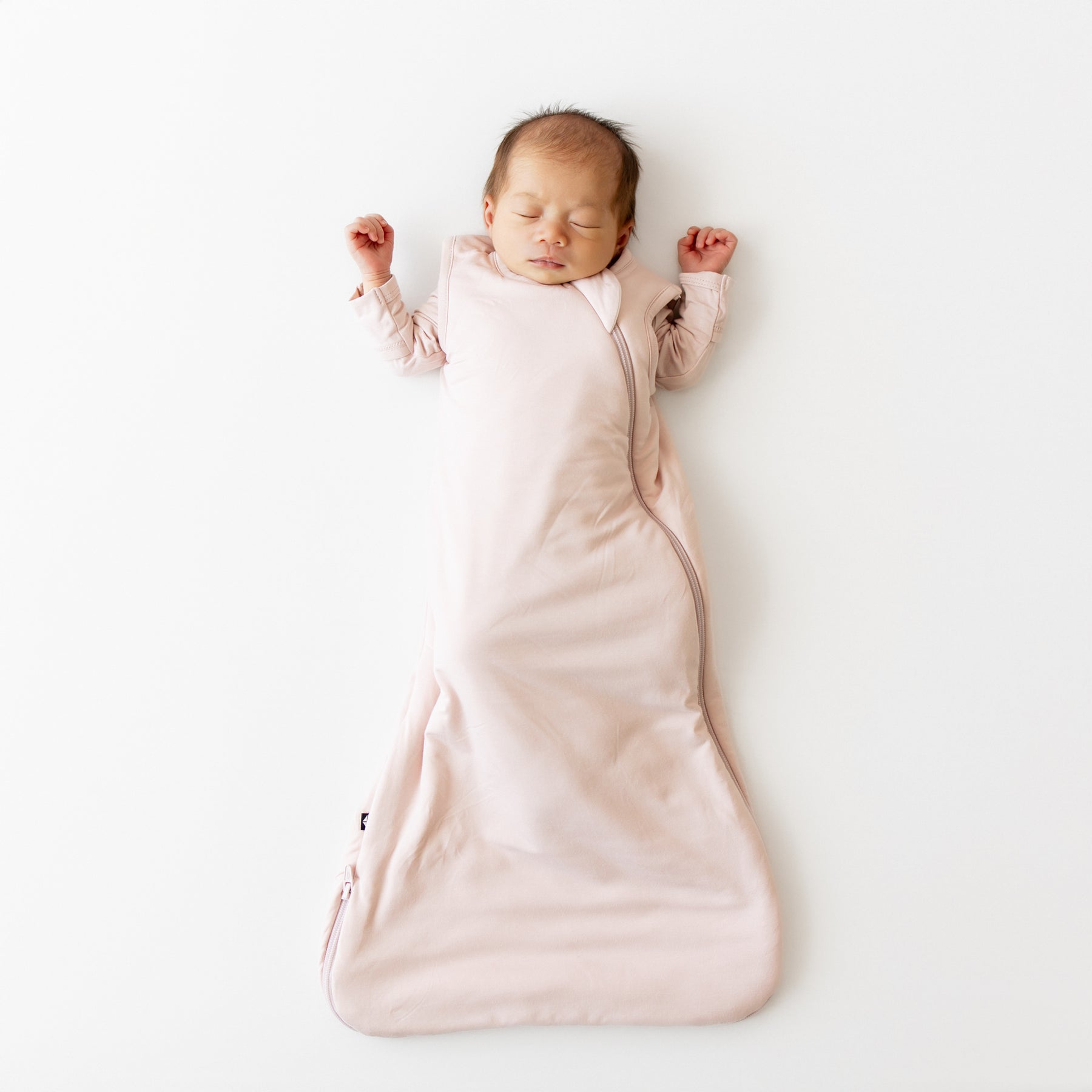 Baby sleeping in a pink sleep bag on a white background