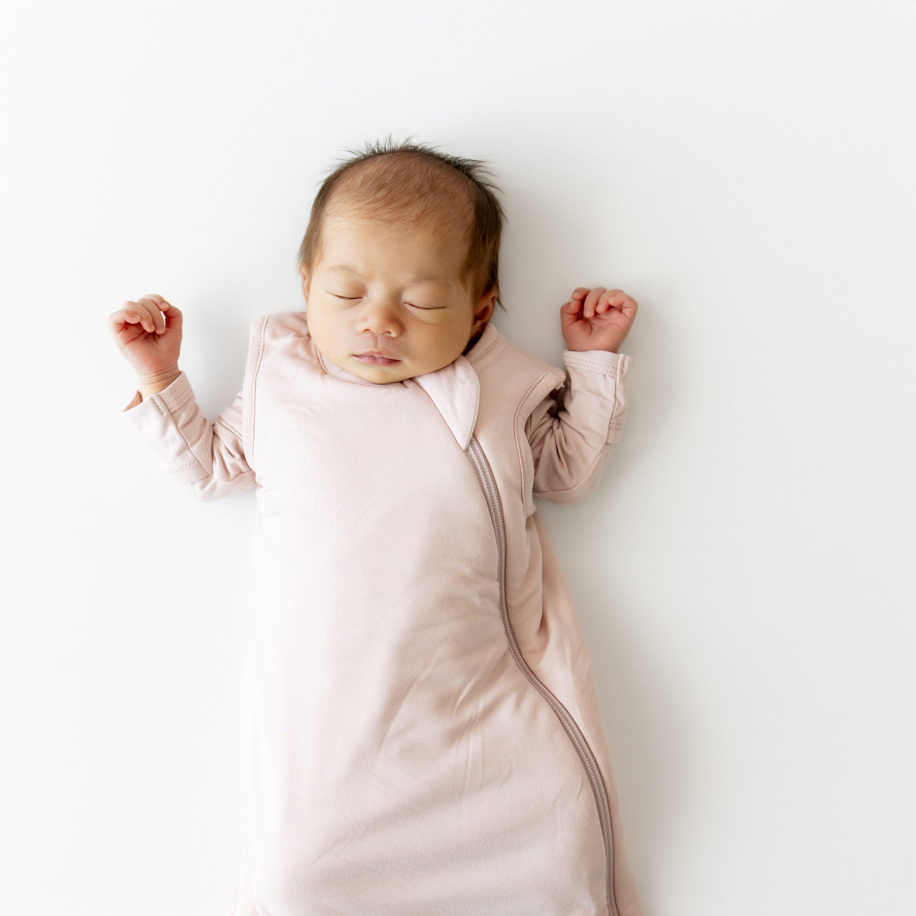 Newborn baby sleeping in a pink sleep bag on a white background