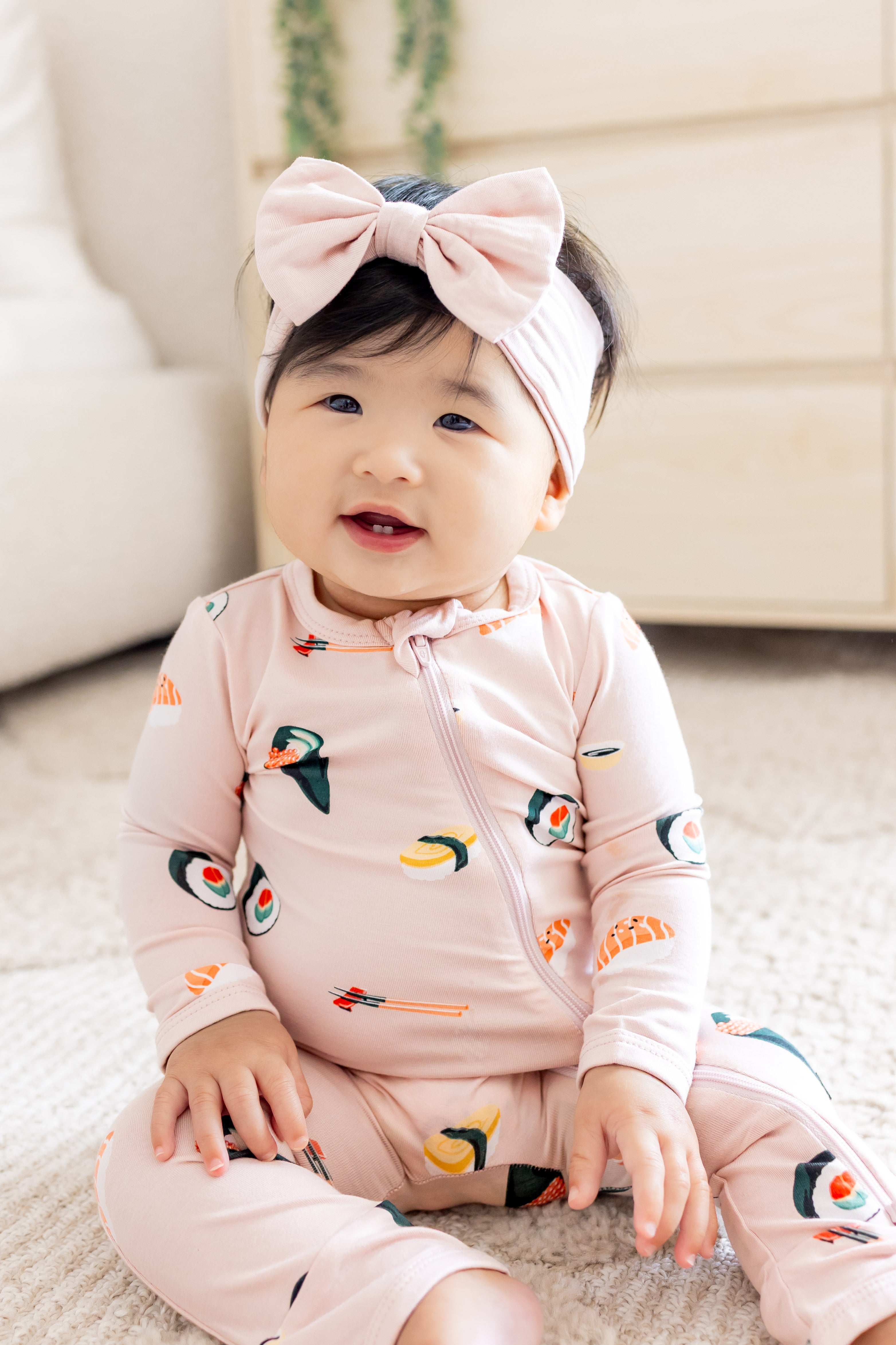 Baby sitting up in blush sushi zipper romper and pink bow