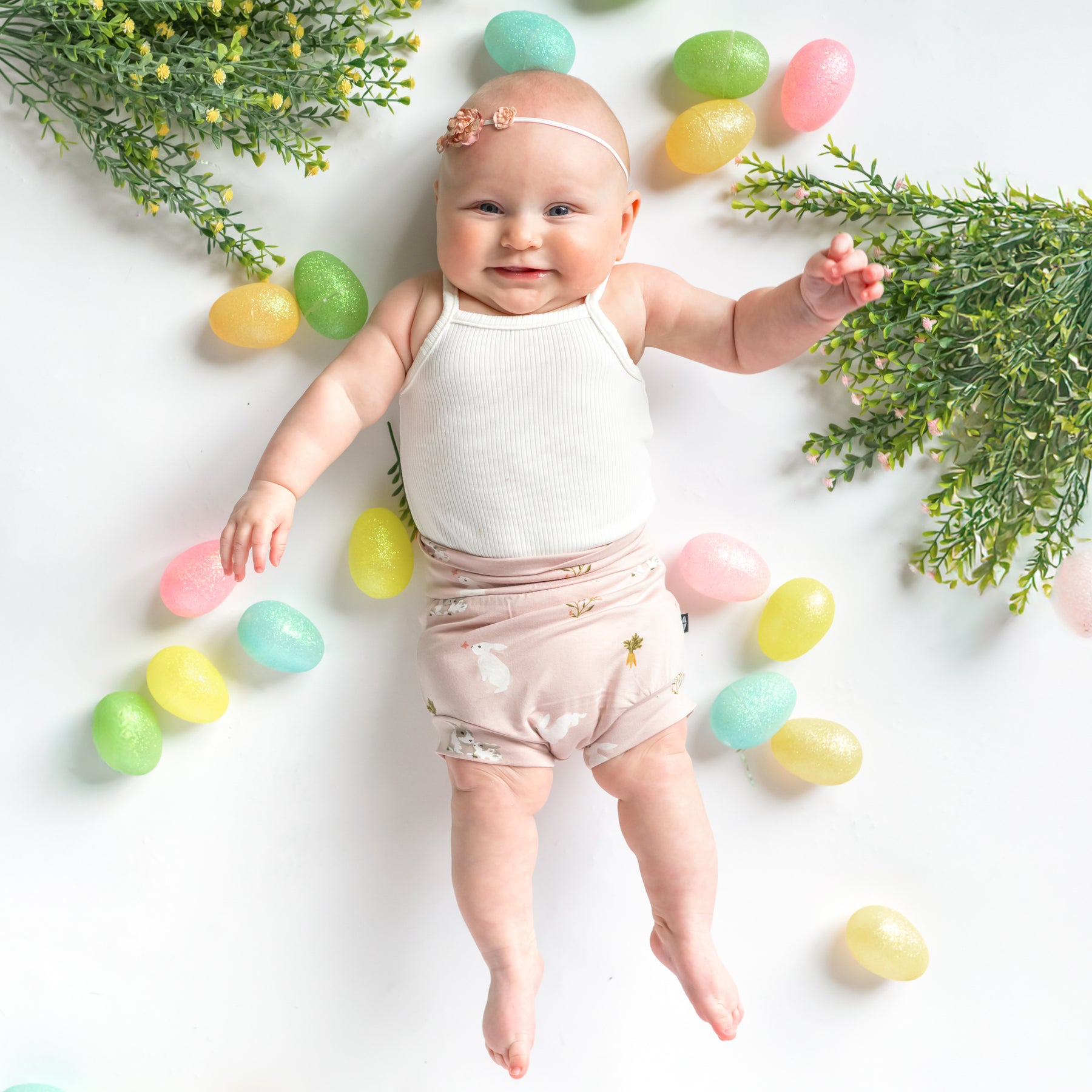 Baby in Bummies in Blush Rabbit surrounded by easter eggs 