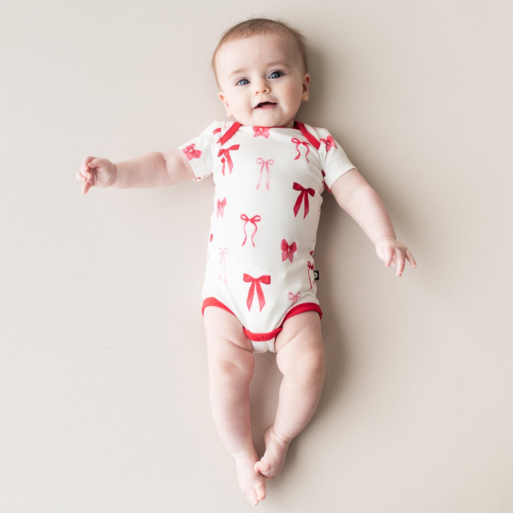 Infant laying on a light neutral surface wearing the Bodysuit in Small Love Bow