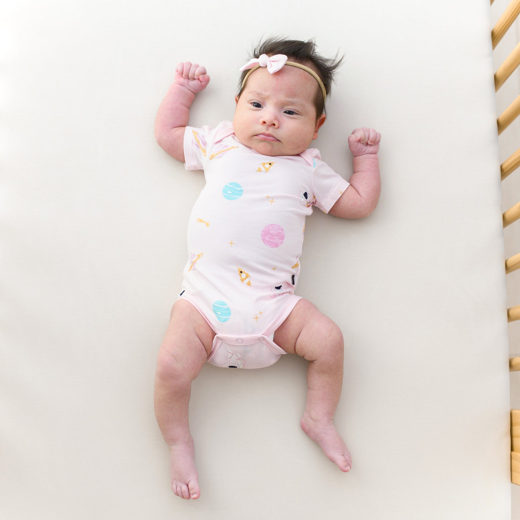 baby wearing short sleeve sakura space bodysuit laying in a crib