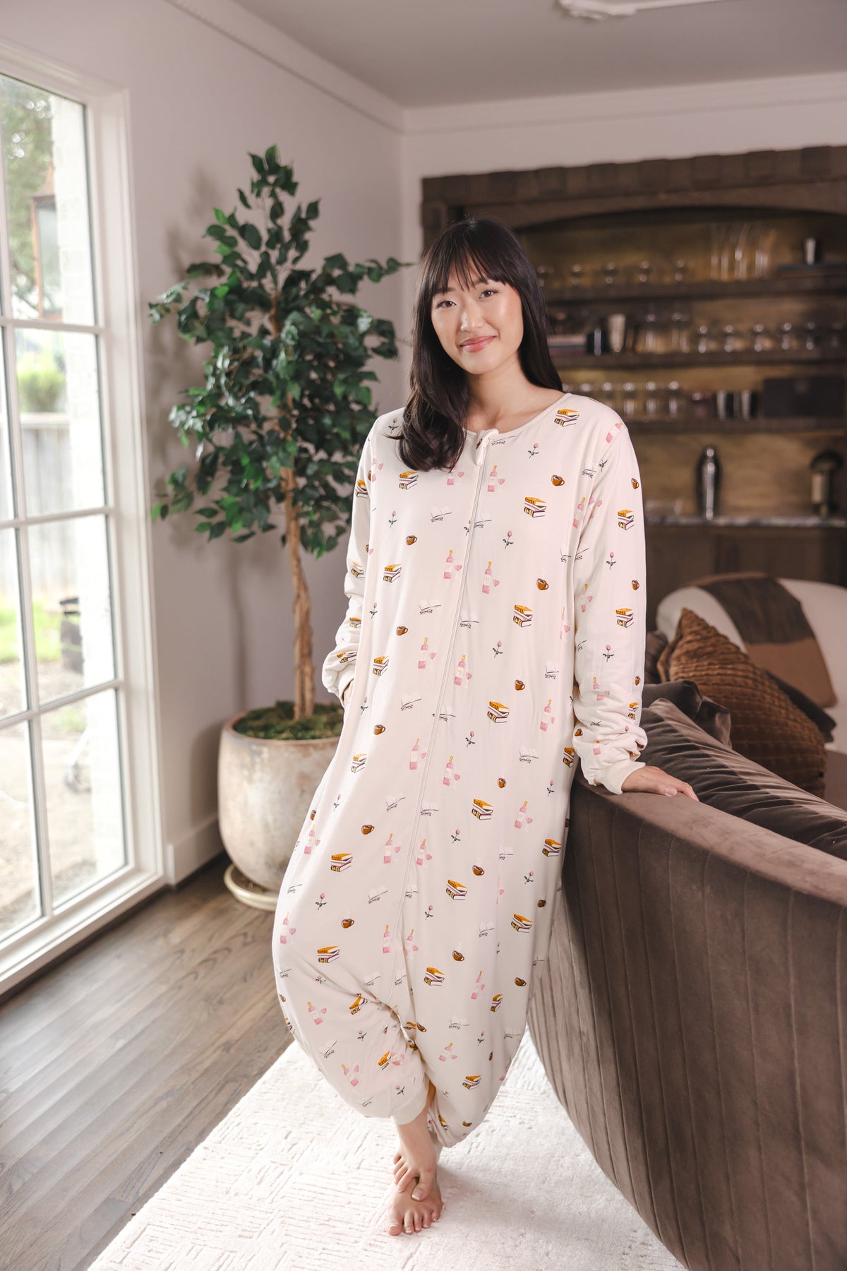 Modal standing in a living room wearing Beige Long Sleeve Adult Sleep Bag Walker in Book Club print