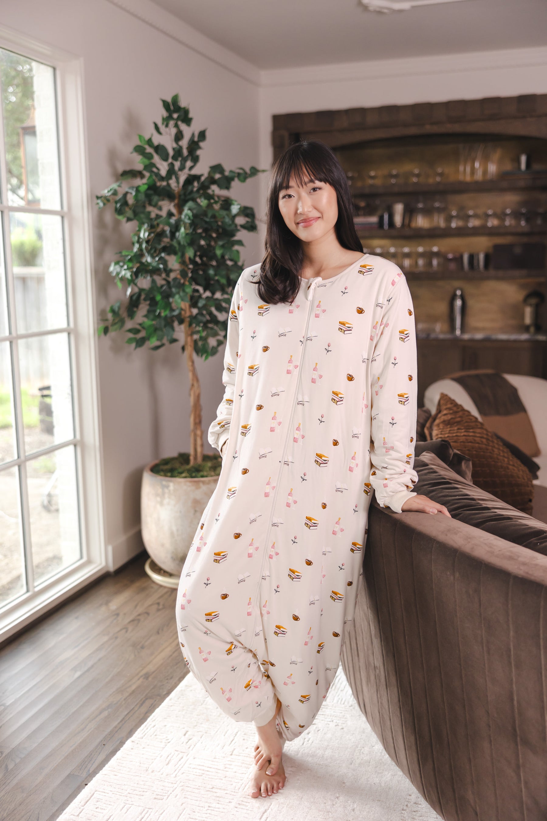 Modal standing in a living room wearing Beige Long Sleeve Adult Sleep Bag Walker in Book Club print