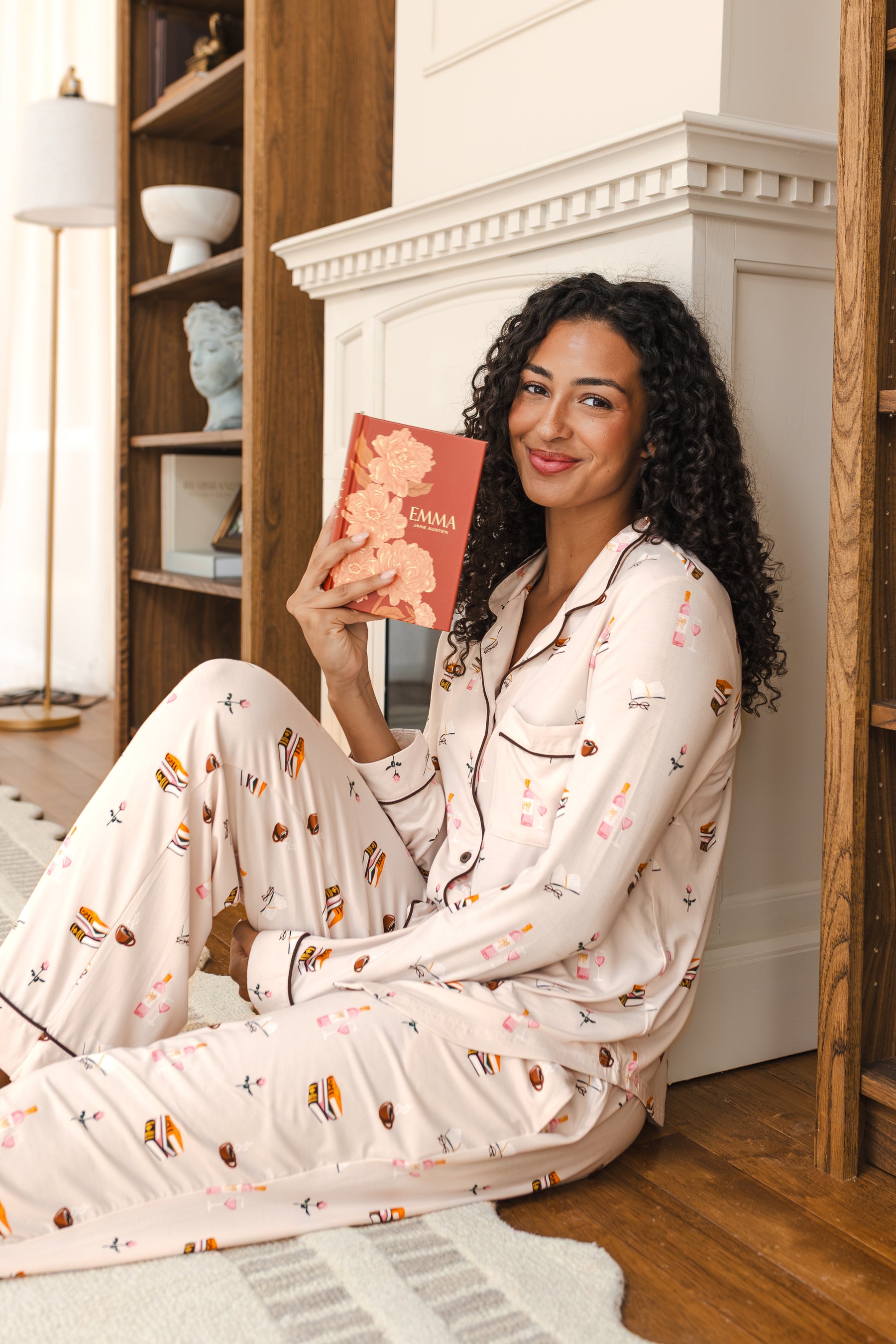 Modal wearing Long-Sleeved Women's Pajama Set in Book Club print sitting with a book in a living room