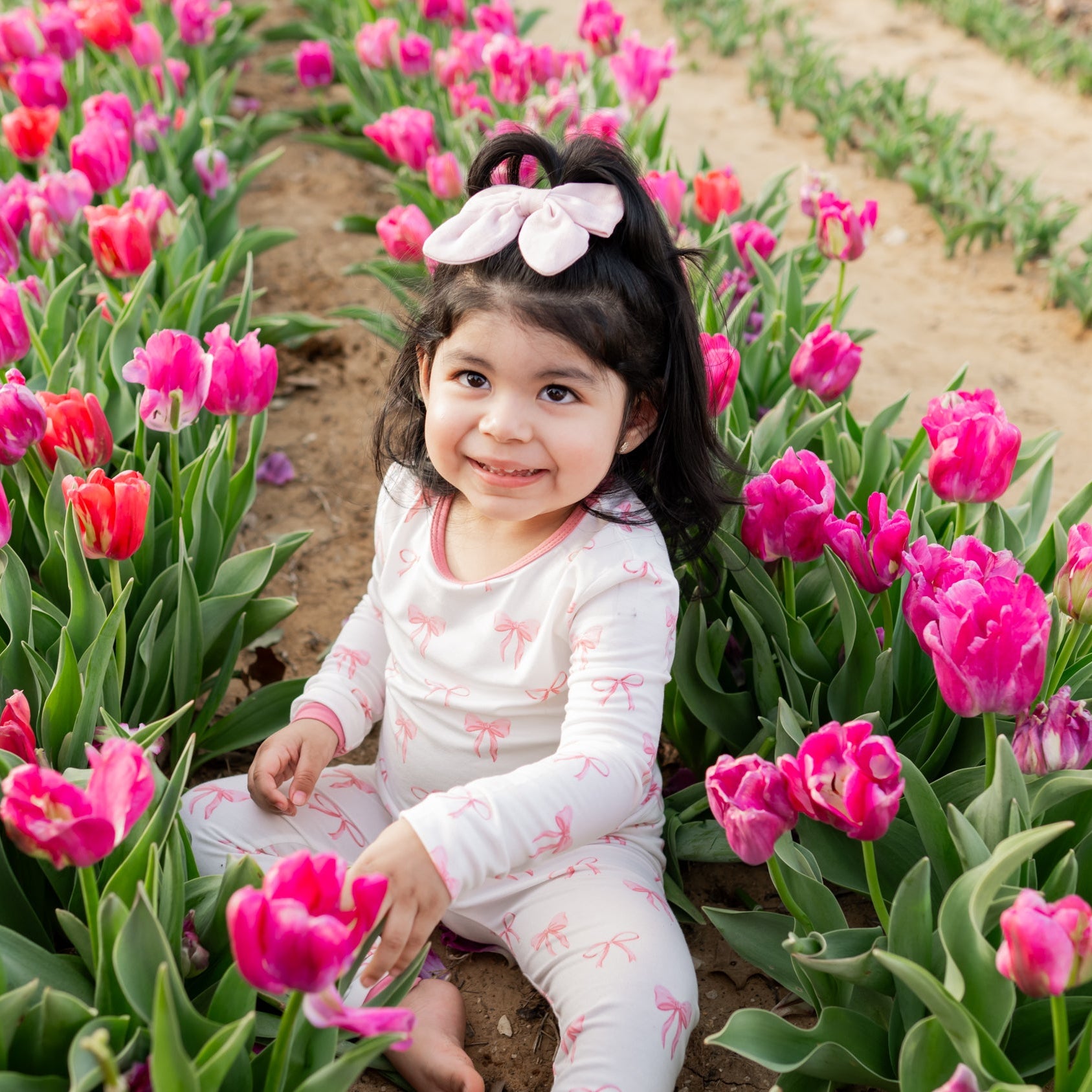 Young girl sitting among pink tulips in a field