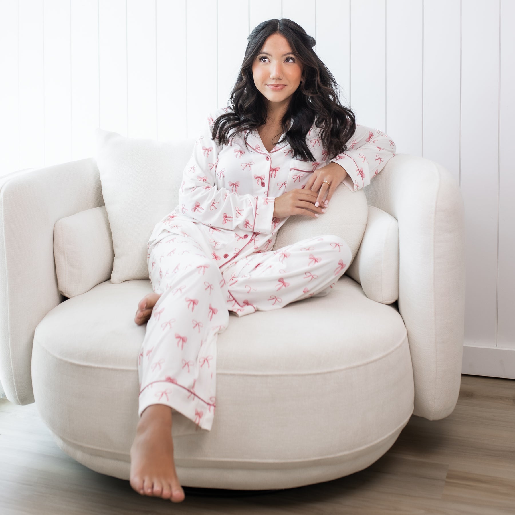 Female sitting on a round white sofa wearing the Long-Sleeved Women's Pajama Set in Bow