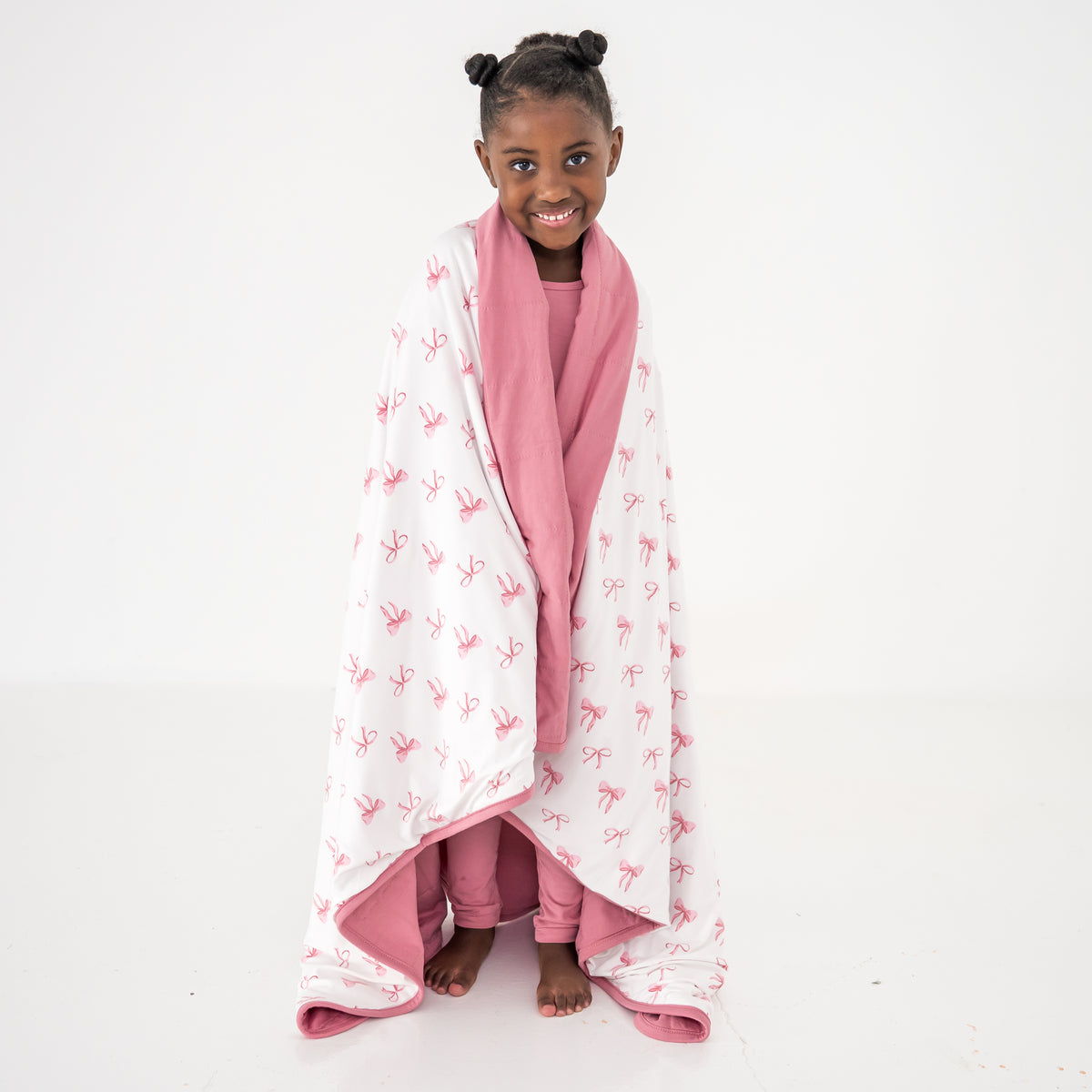 Toddler wrapped in a blanket that has a pink bow pattern on a white background with pink trim