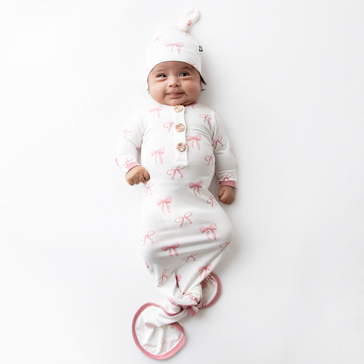 Infant laying on a white surface wearing the Knotted Gown with Hat Set in Bow