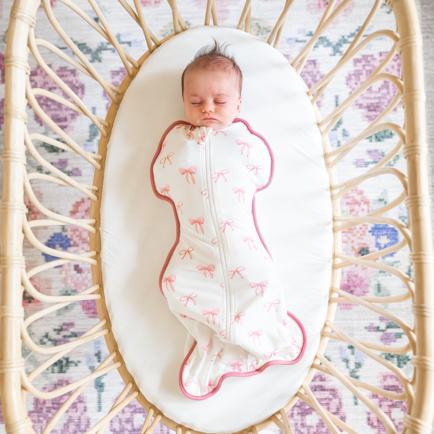 Sleeping newborn laying in a mini crib wearing the Swaddle Bag in Bow 0.5
