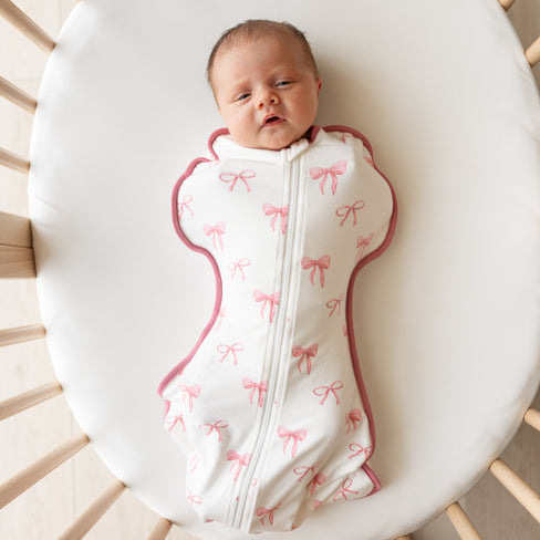 Baby wearing Swaddle Bag in Bow 0.5 in a oval mini crib
