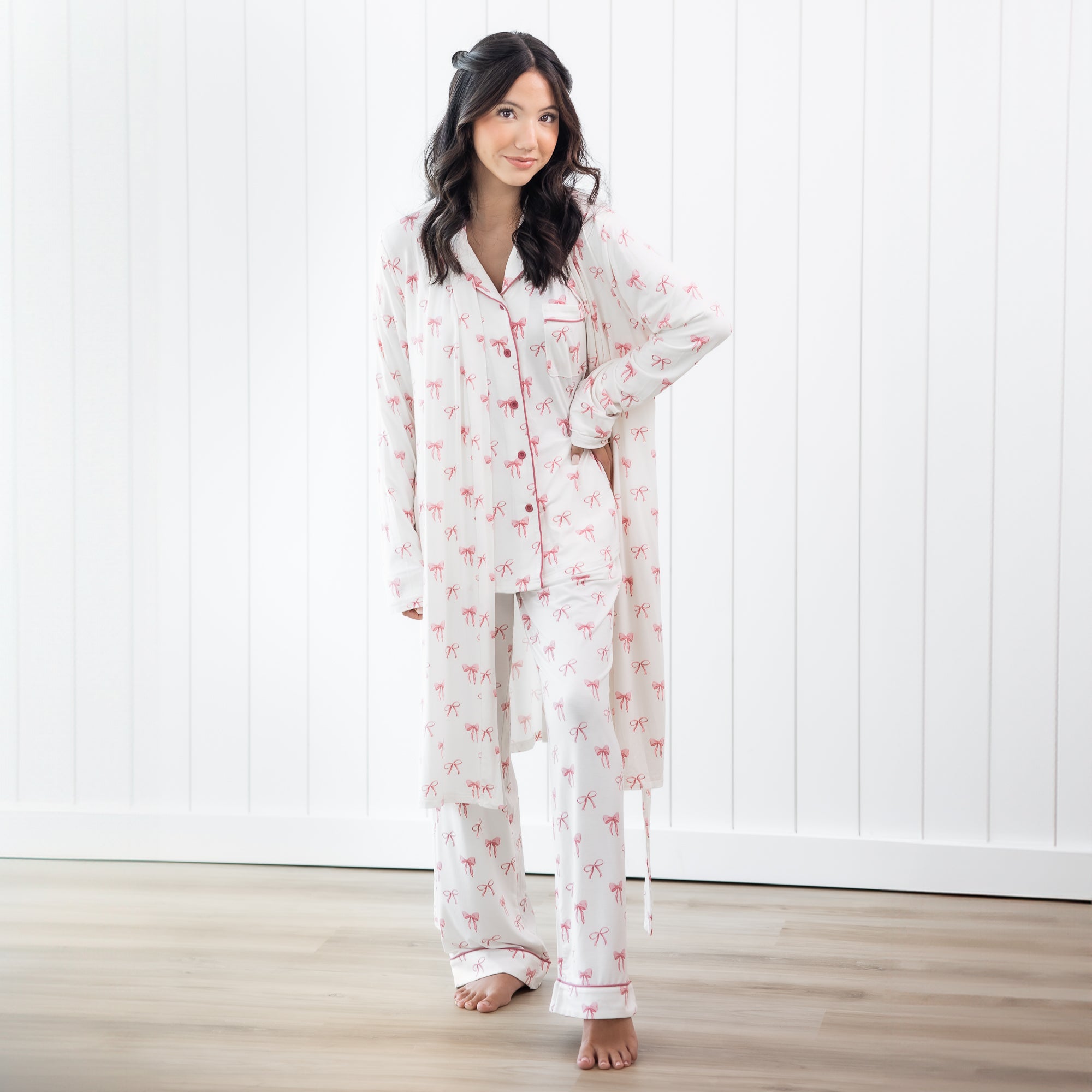 Woman wearing white long sleeve button up pajamas and robe with a pink bow print 