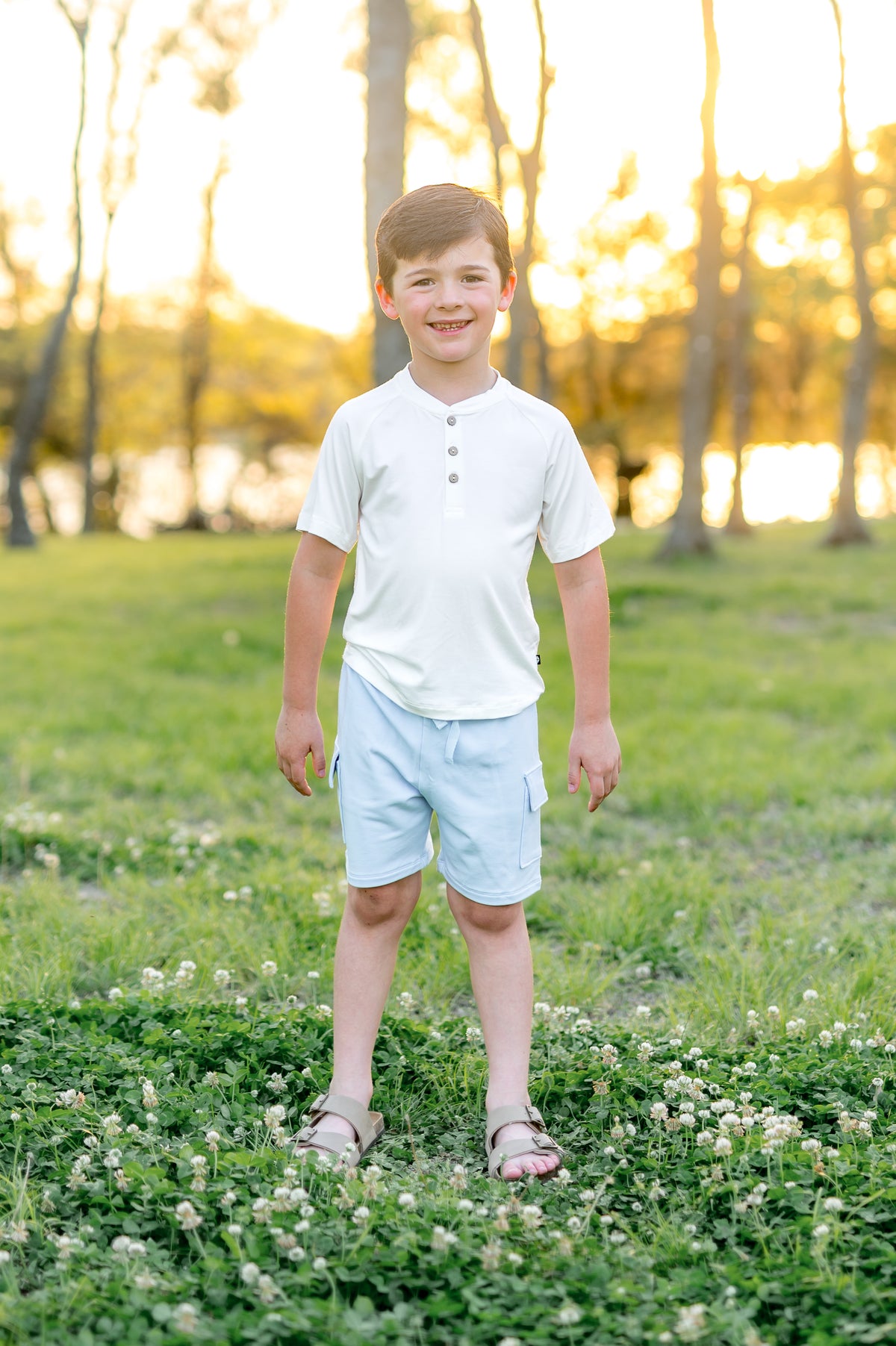Young boy standing in a grass field wearing the Cargo Short in Breeze with a white short sleeve henley tee