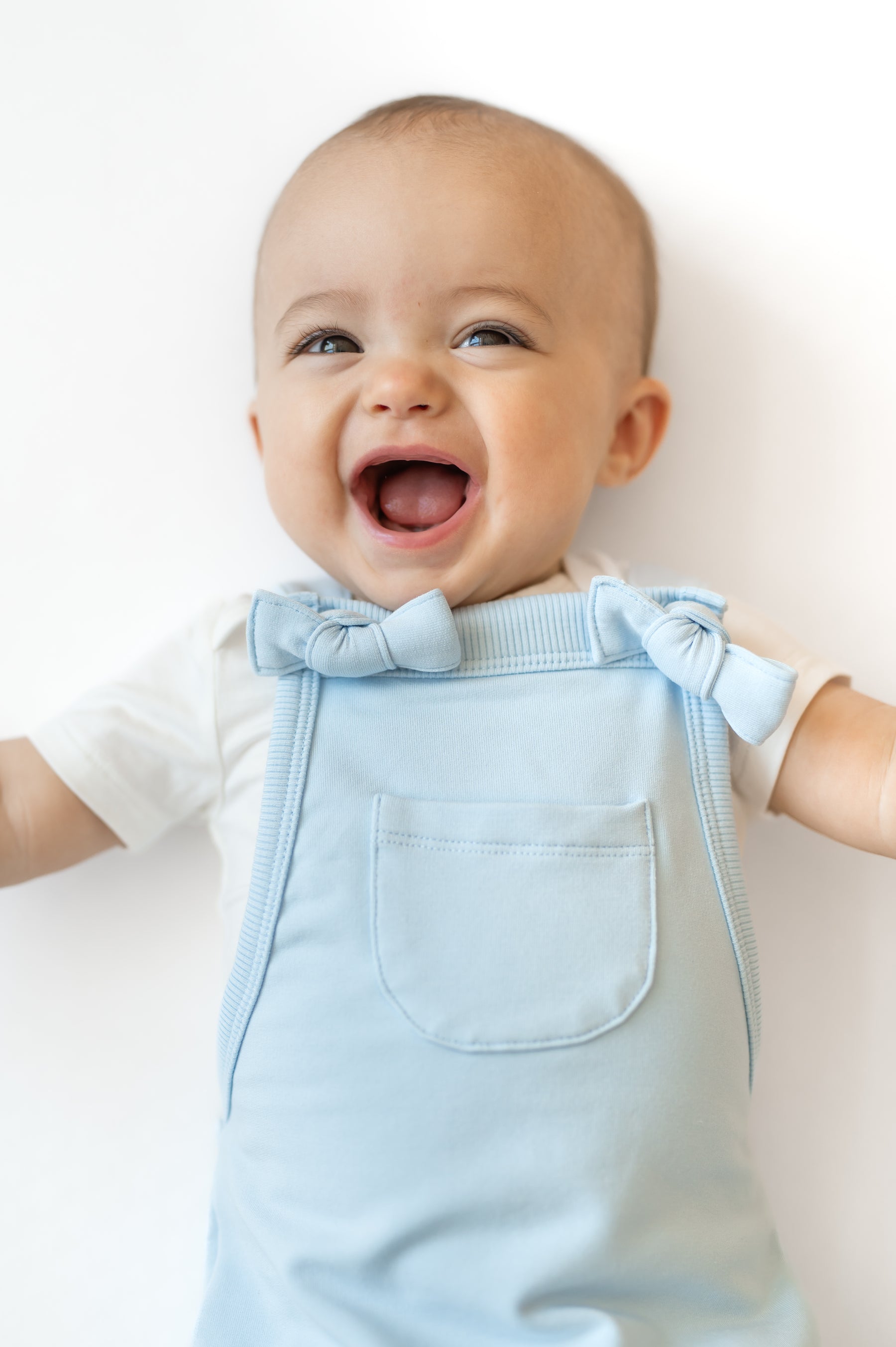 Close up of smiling infant wearing the Overall in Breeze showing the front pocket