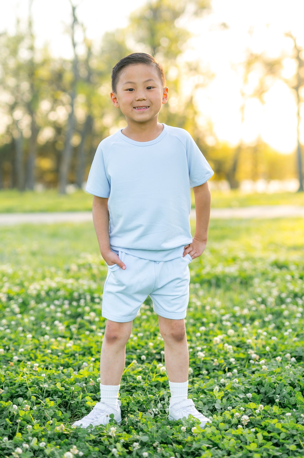 Young boy standing in a grass field wearing the Short Sleeve Jogger Set in Breeze with his hands in the pockets of the shorts