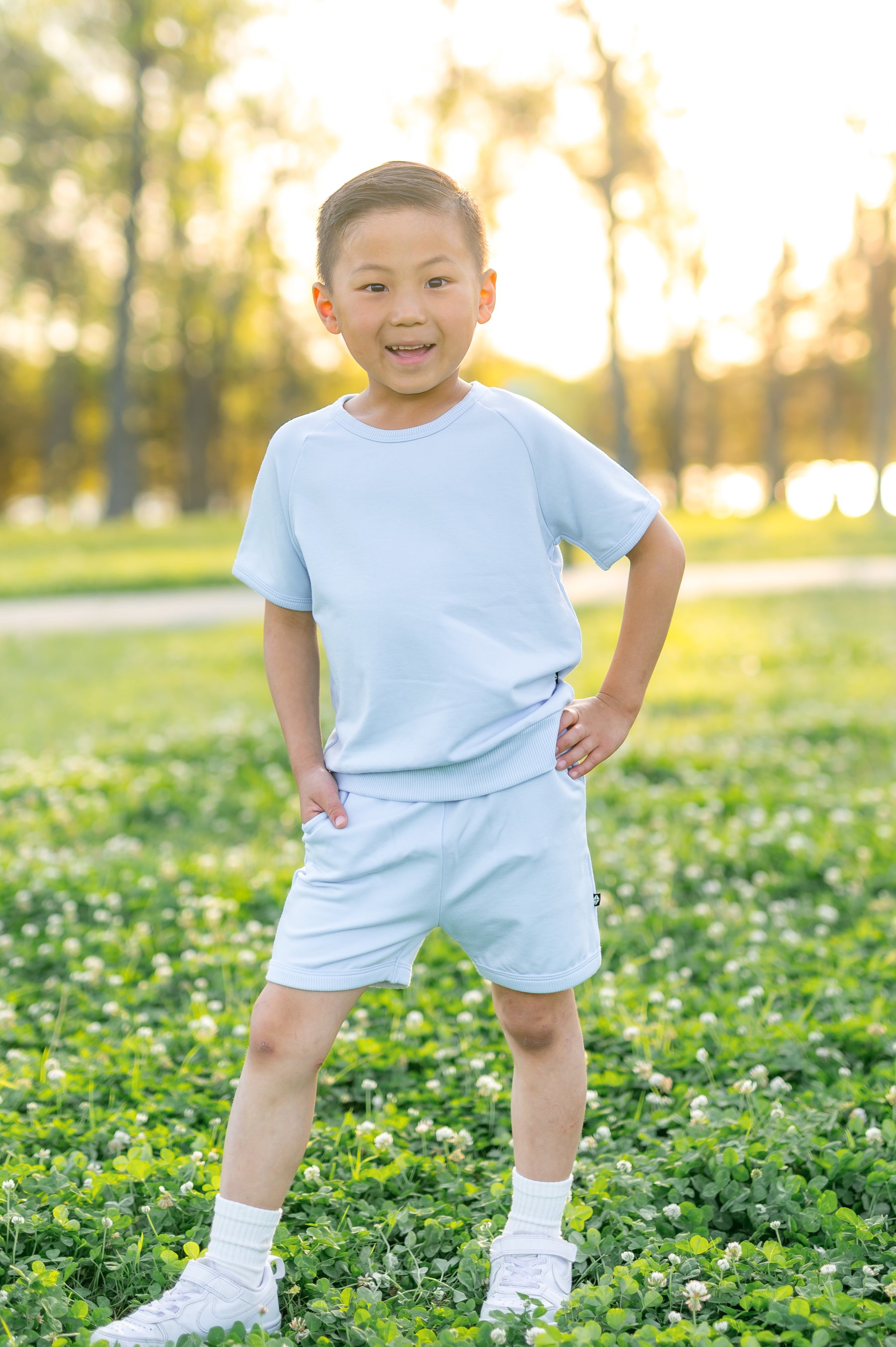 Young boy posing standing in a grass field wearing the Short Sleeve Jogger Set in Breeze 