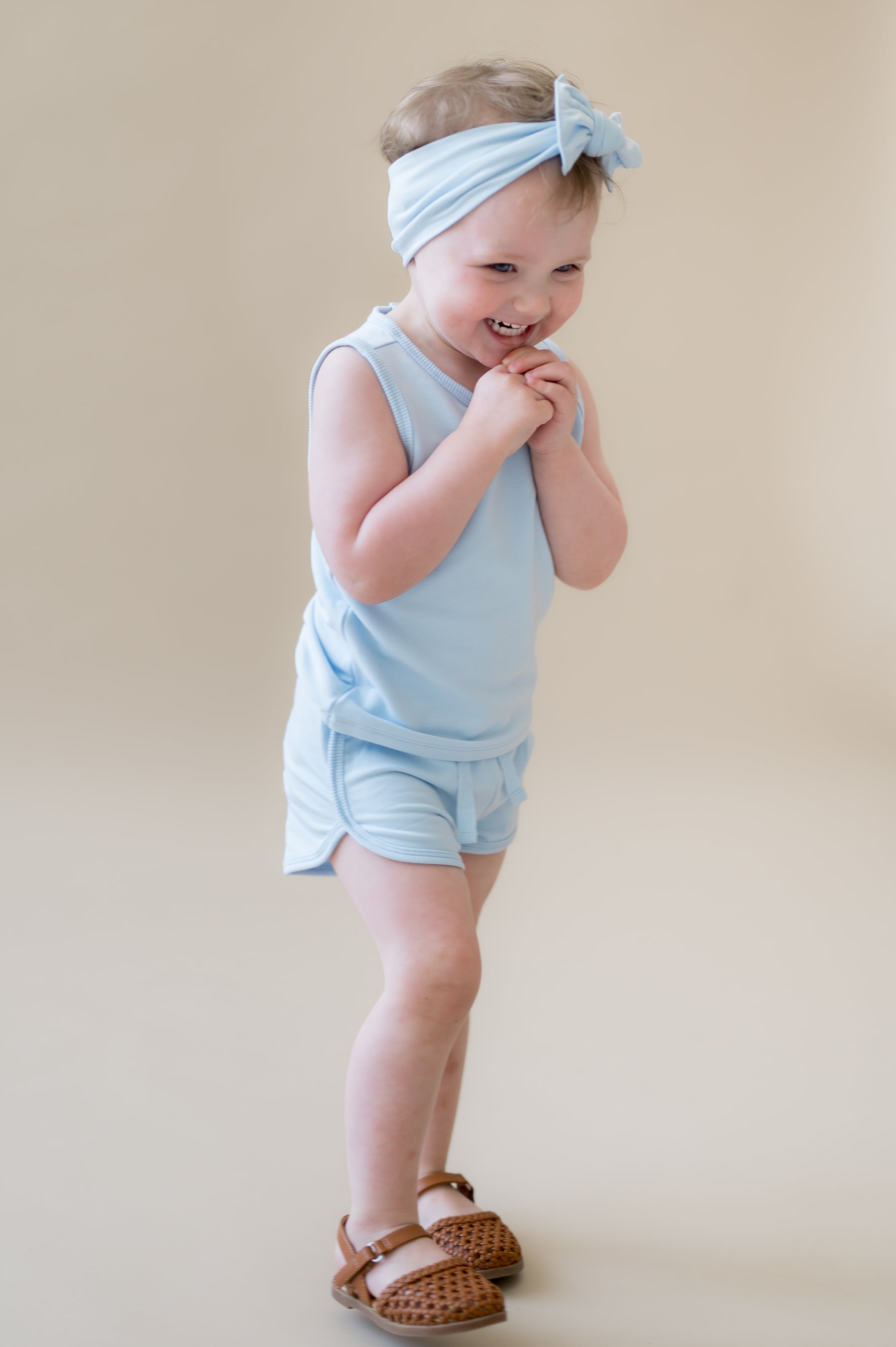 Young smiling girl walking wearing the Tank Jogger Set in Breeze in front of a light beige background