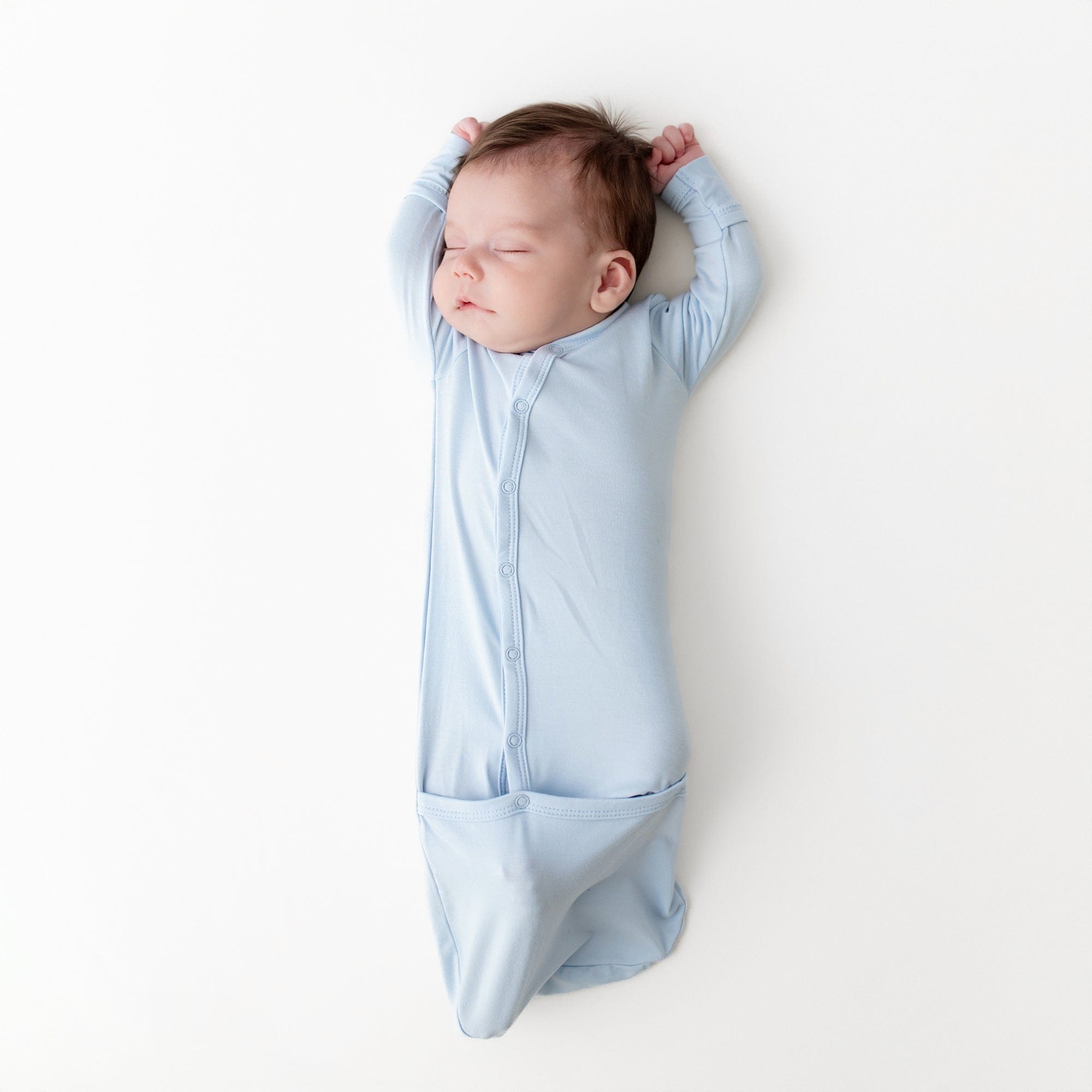 Sleeping newborn wearing the Bundler in Breeze laying on a light neutral surface