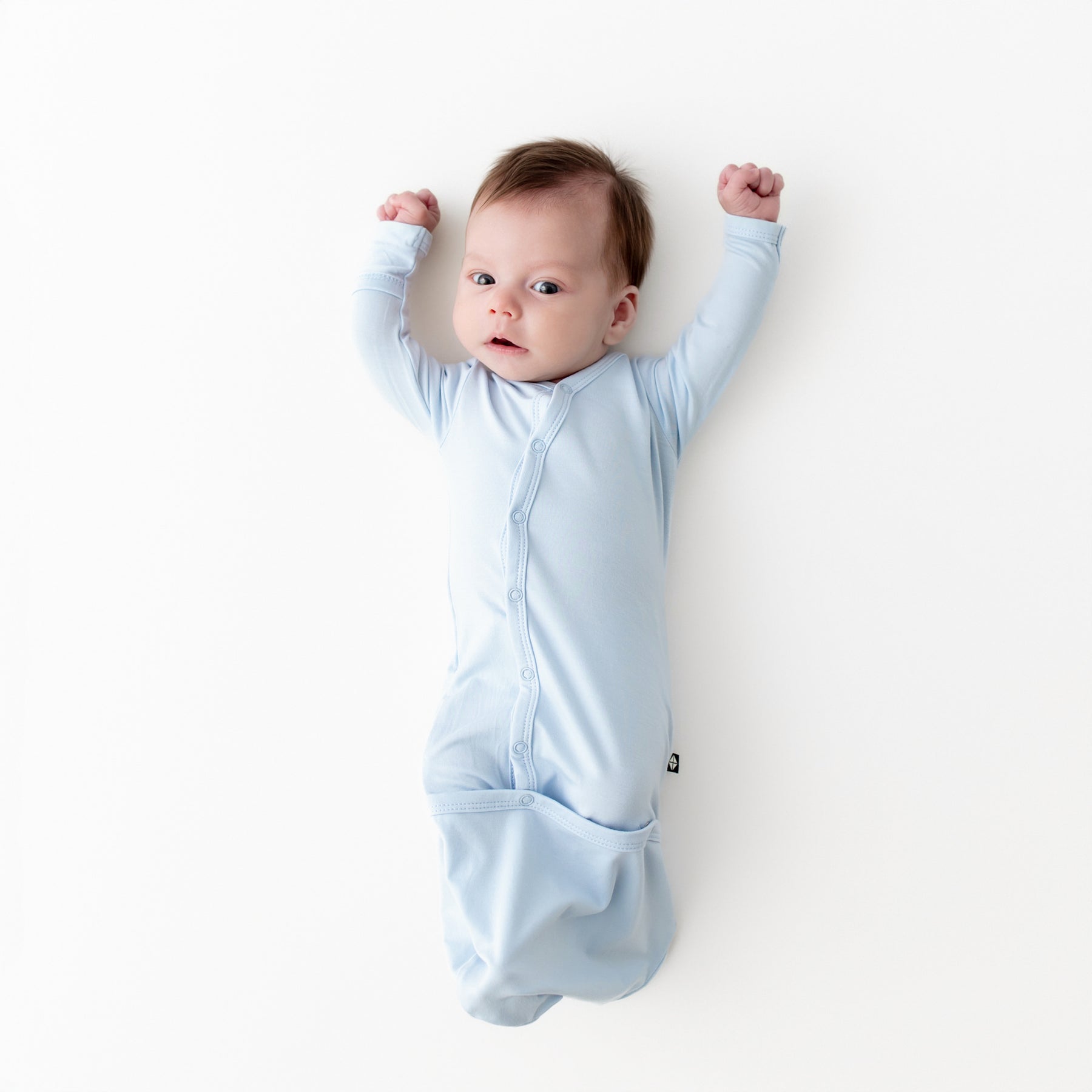 Newborn laying on a white surface wearing the Bundler in Breeze