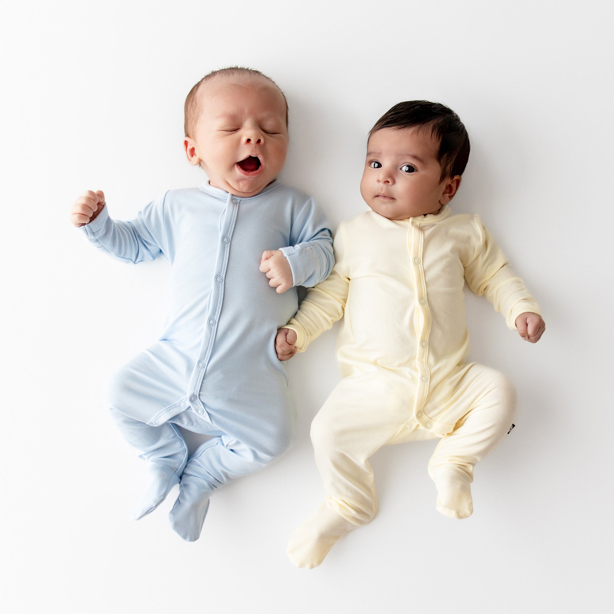 Two infants laying side by side wearing the Footie in Breeze and Chamomile
