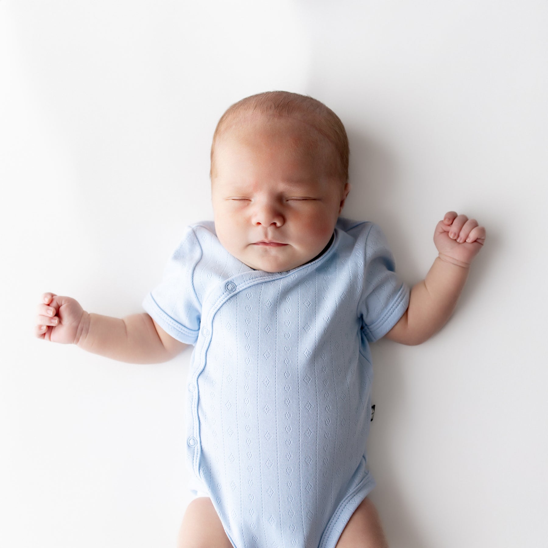 Close up of sleeping newborn wearing the Pointelle Kimono Bodysuit in Breeze