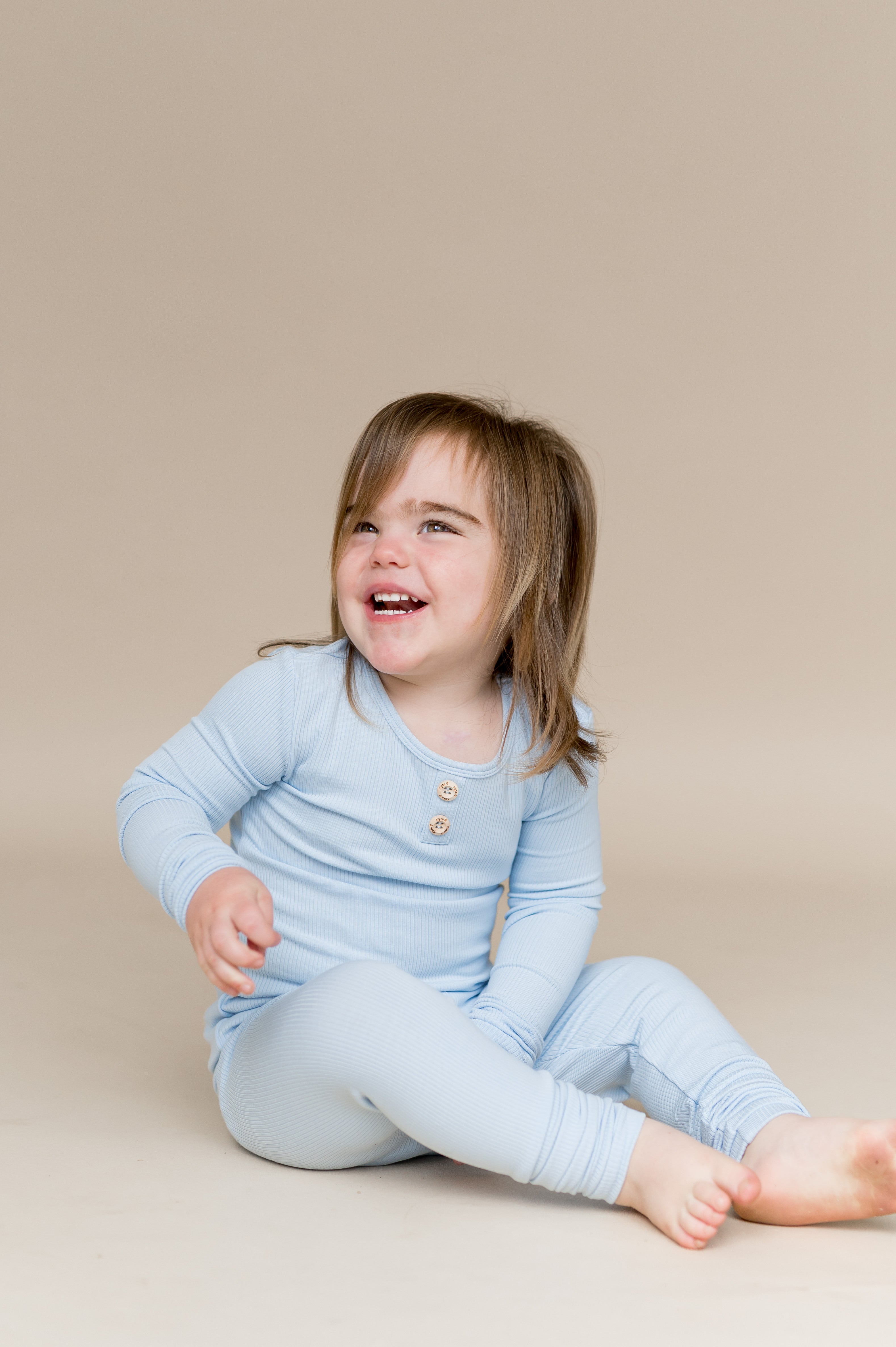 Young smiling child sitting on the floor wearing the Ribbed Henley Set in Breeze