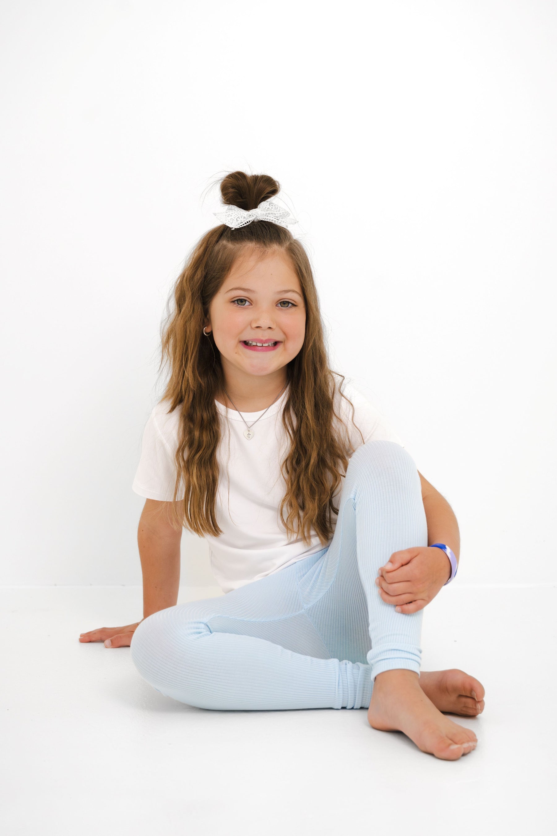 Young girl sitting on the floor wearing the Ribbed Leggings in Breeze with a white shirt