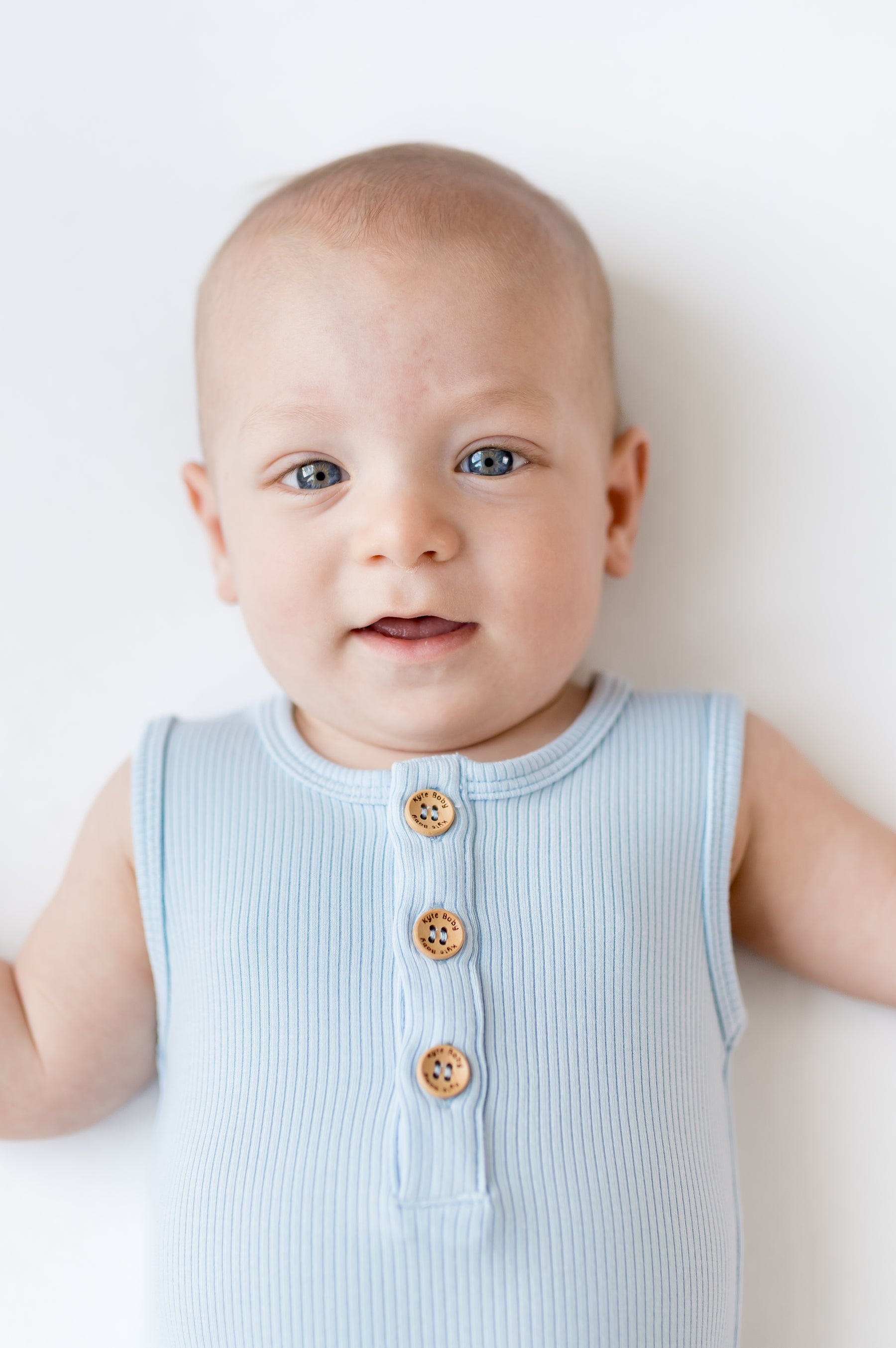 Close up of infant wearing the Ribbed Sleeveless Shortall in Breeze showing the engraved Kyte Baby wooden buttons
