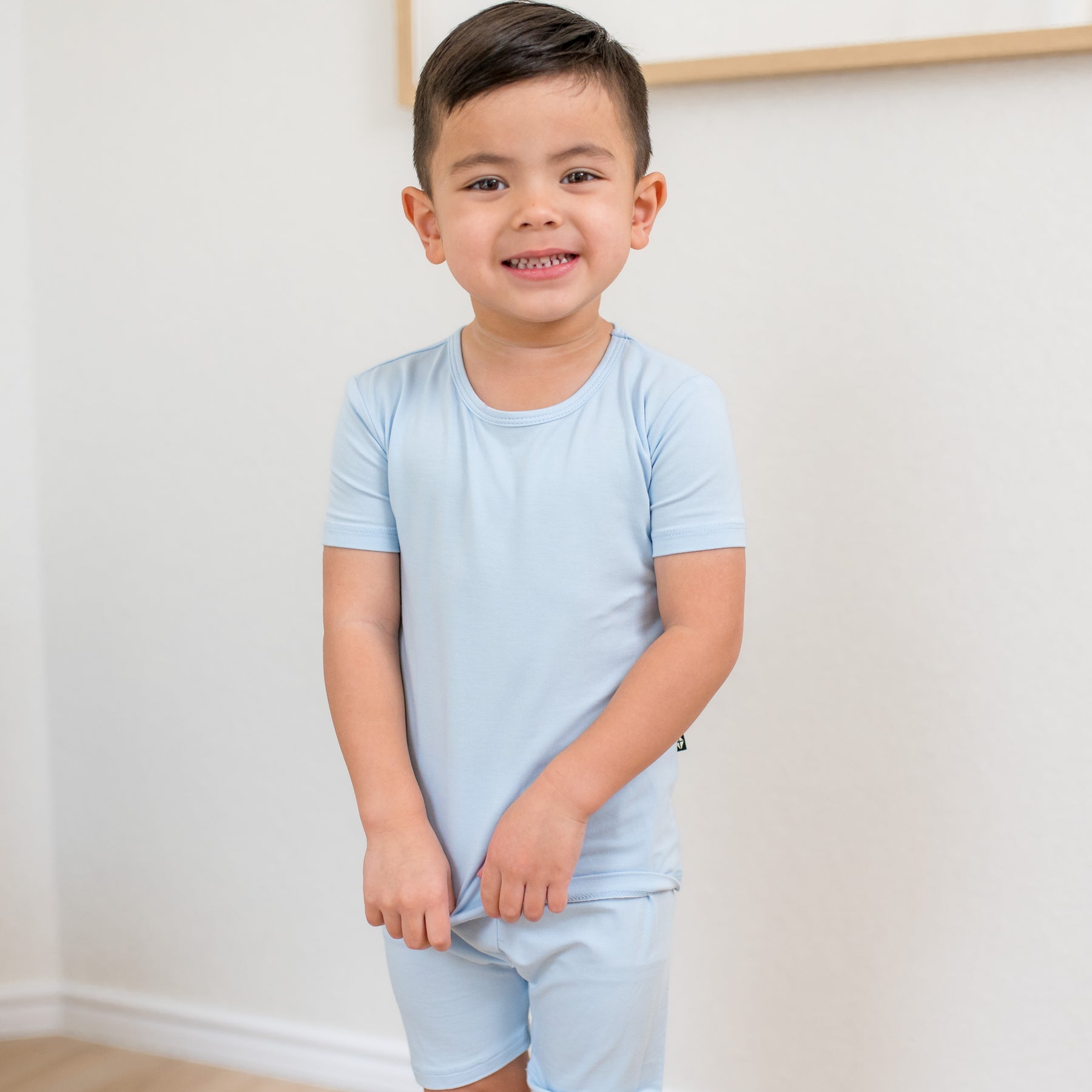 Young boy standing in front of a white wall wearing the Short Sleeve Pajamas in Breeze