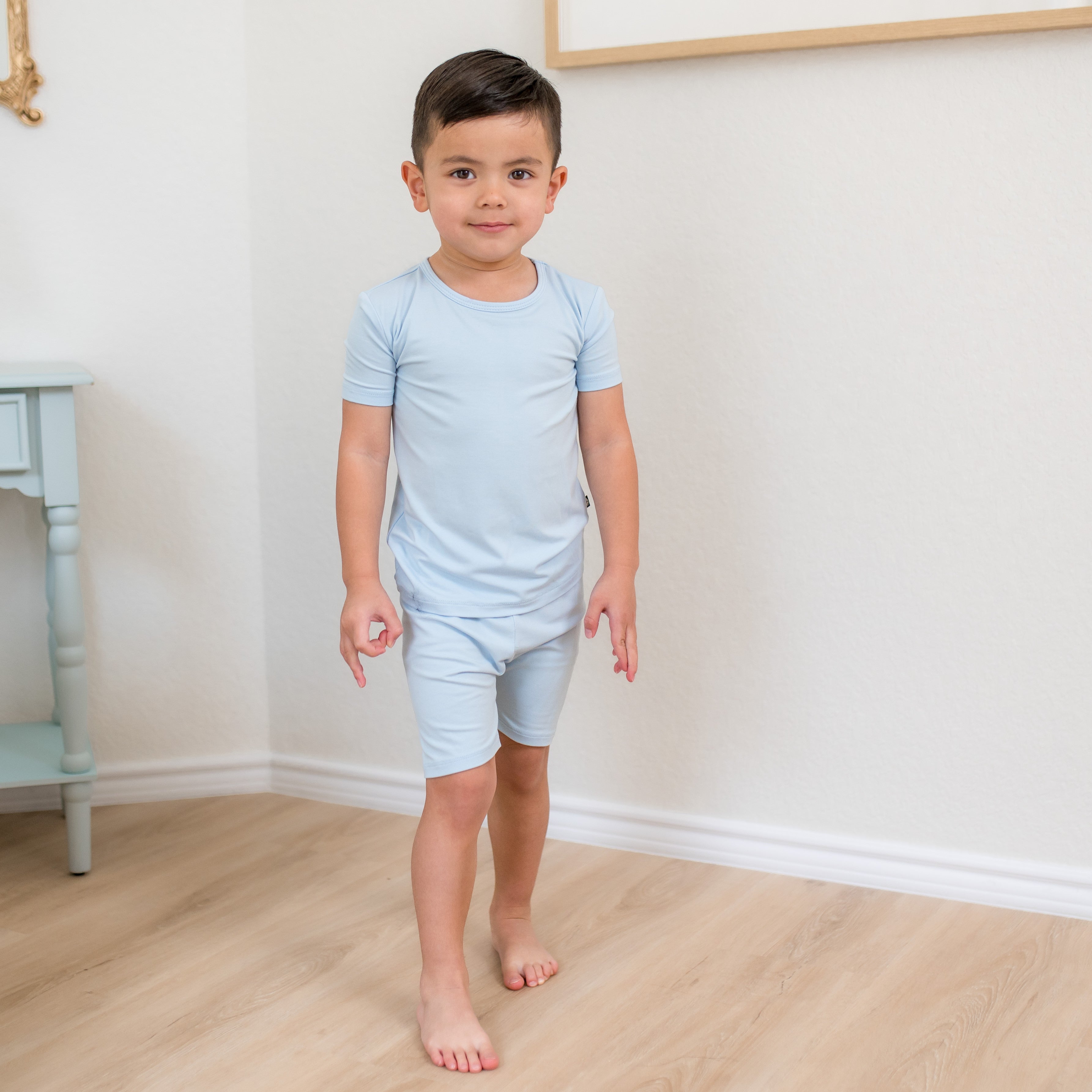 Young boy walking in front of  a white wall wearing the Short Sleeve Pajamas in Breeze