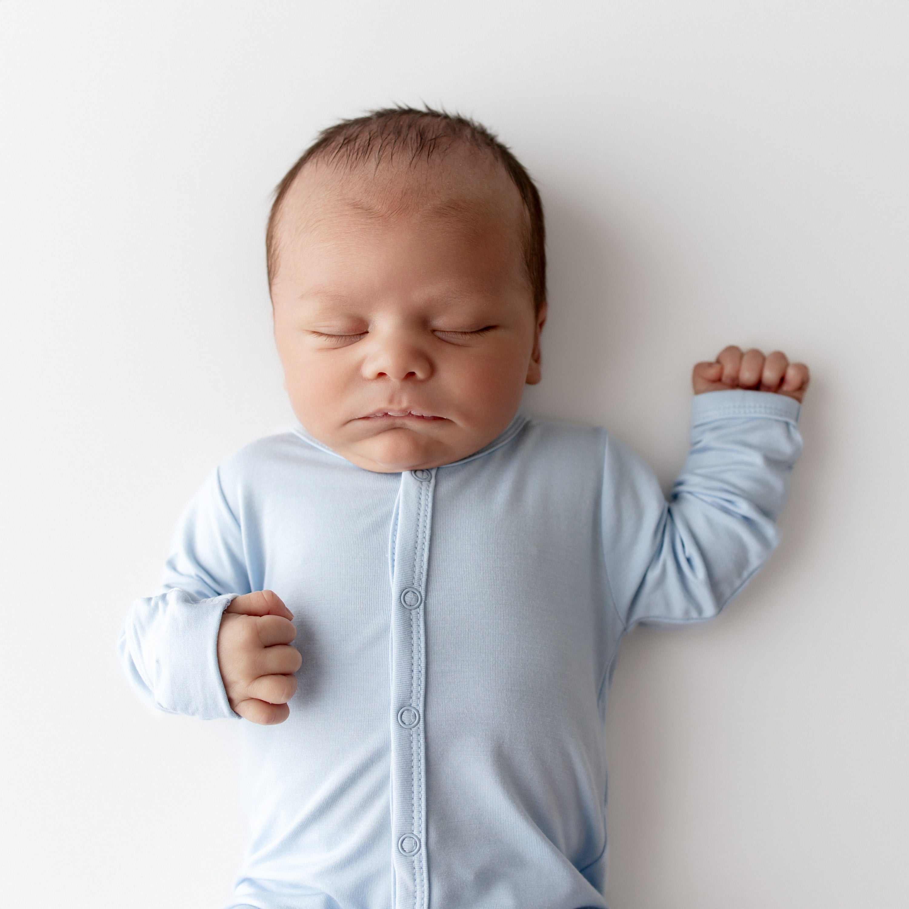 Newborn baby in a light blue footie lying on a white surface