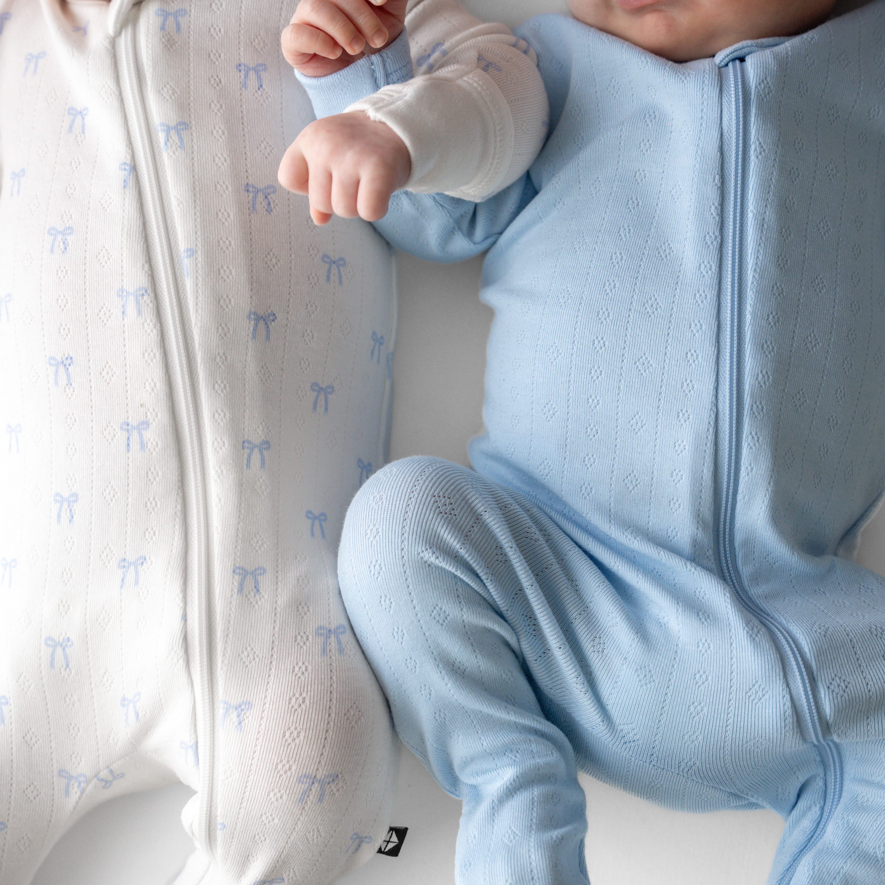 Close up of the fabric on the Pointelle Zippered Footie in Sweet Blue Bow and Breeze on two newborns