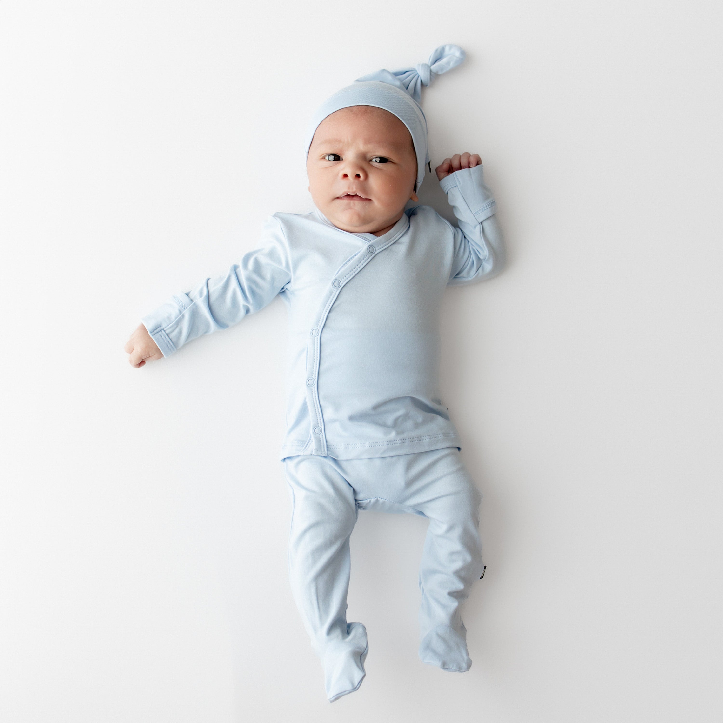 Newborn laying on a light neutral surface wearing the Take Me Home Set with Cap in Breeze