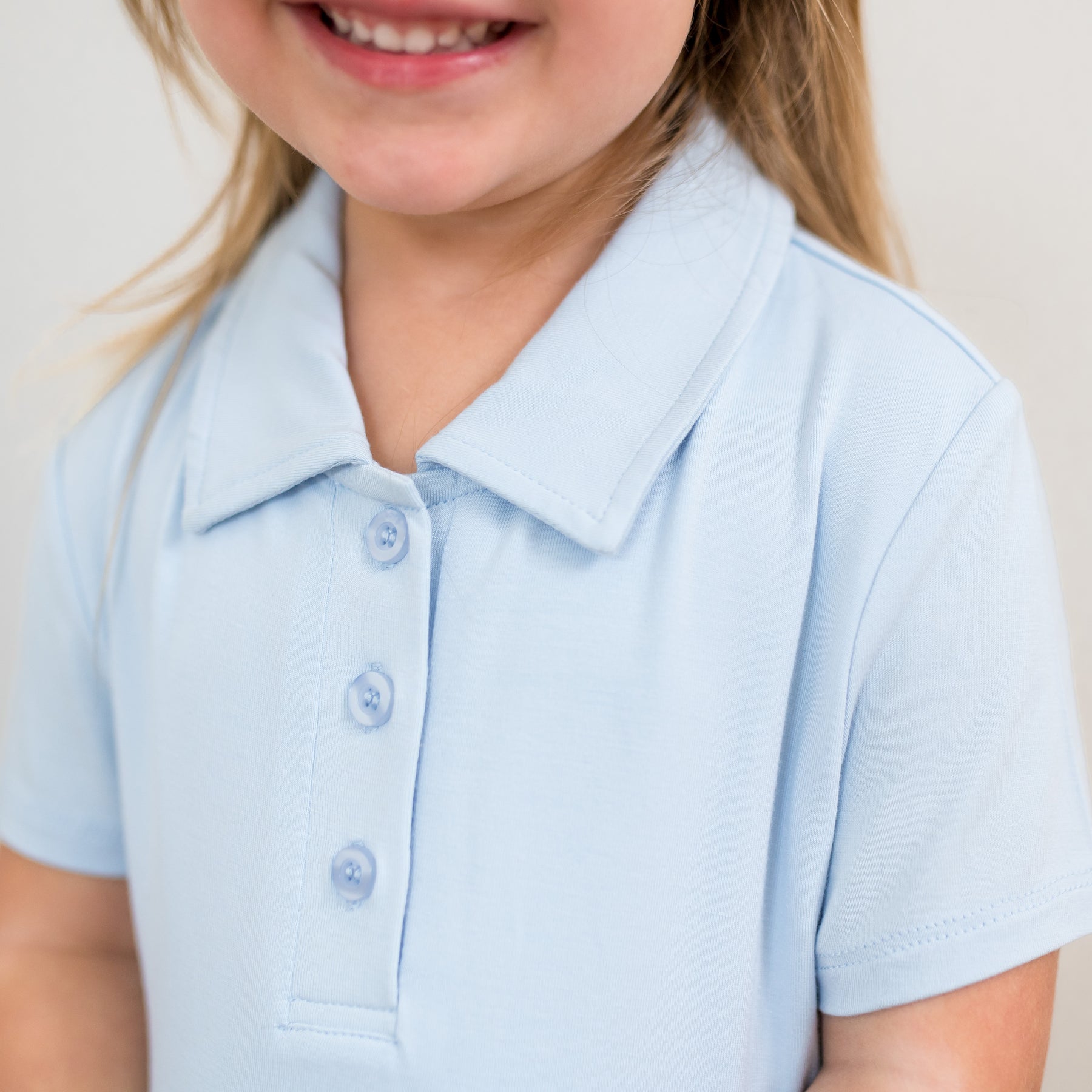 Close-up of a child wearing a light blue polo dress with a plain background