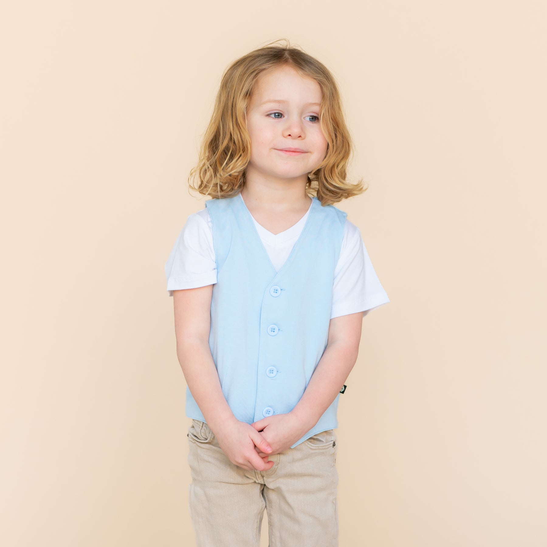 Young model wearing the Tuxedo Vest in Breeze over top of a white vneck paired with khaki pants