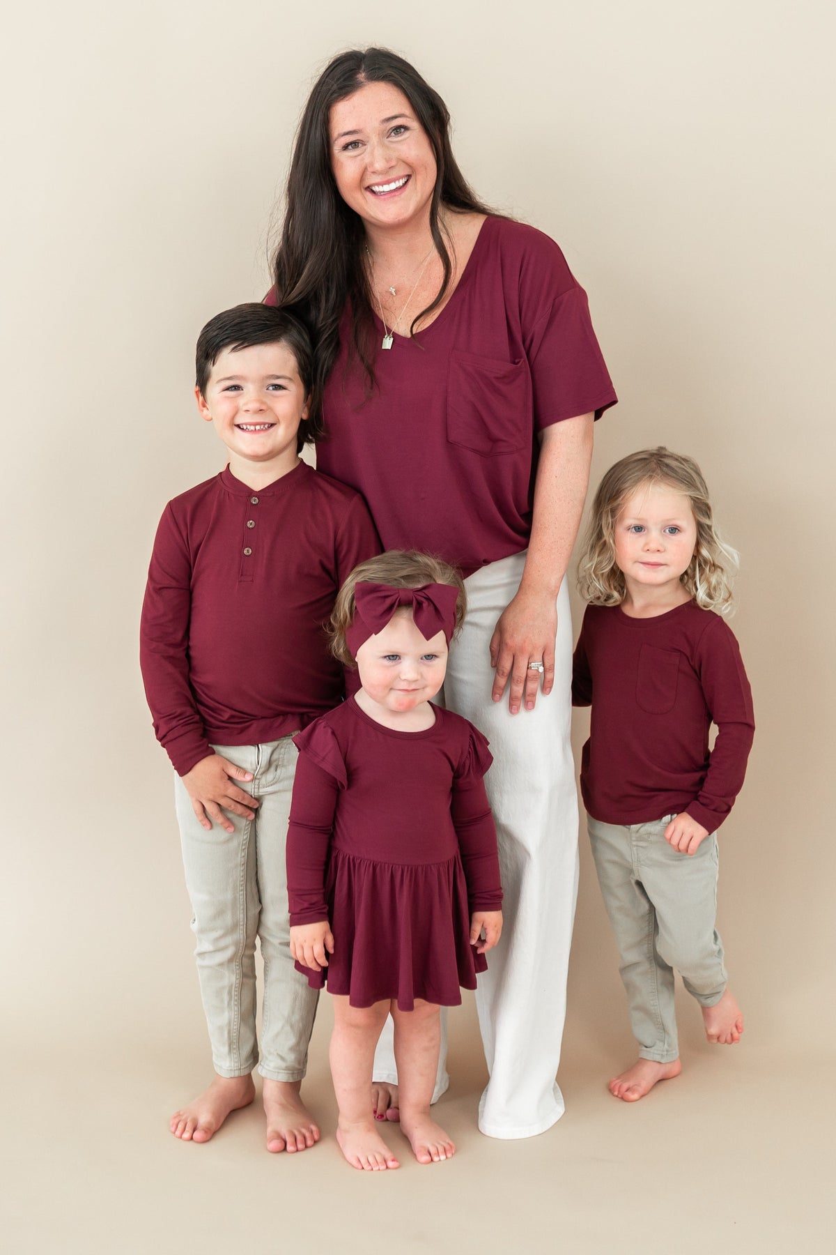 Family matching in Burgundy. Pictured is the Women’s Relaxed Fit V-Neck in Burgundy, Toddler long sleeve henley, twirl bodysuit dress and long sleeve toddler crew neck
