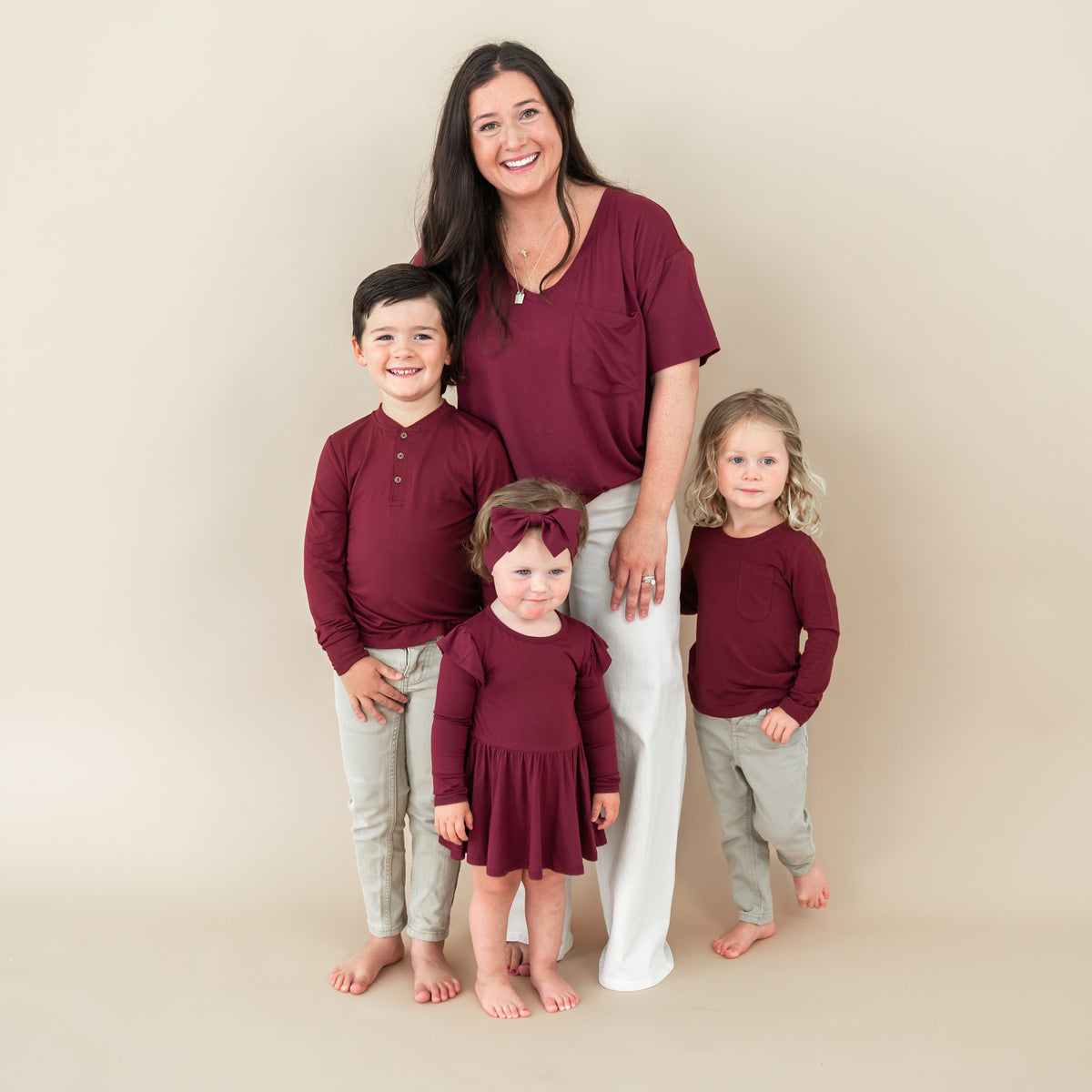 Family matching in Burgundy. Pictured is the Women’s Relaxed Fit V-Neck in Burgundy, Toddler long sleeve henley, twirl bodysuit dress and long sleeve toddler crew neck