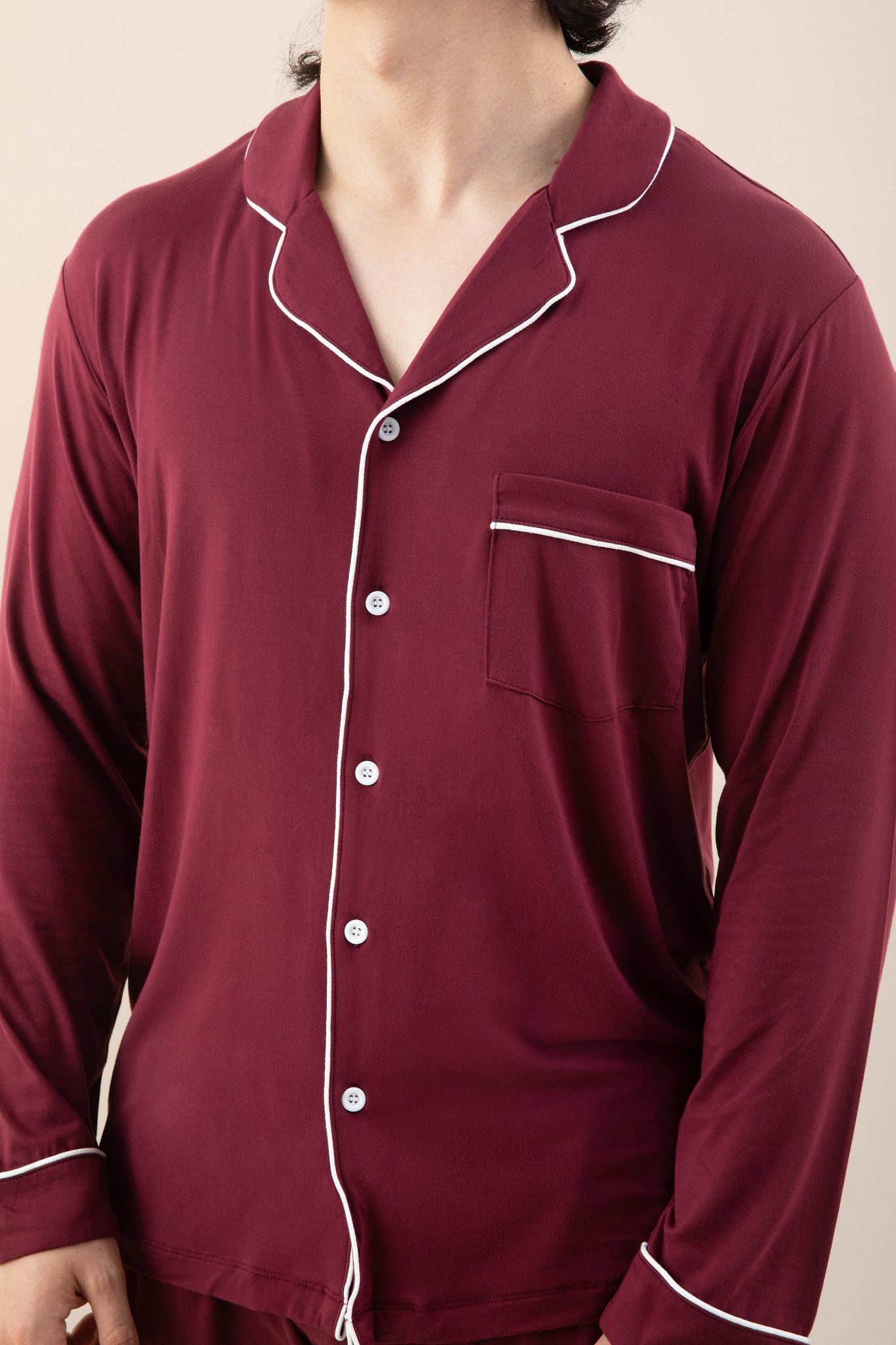Close up of the chest pocket detail, button closure and white trim on the shirt of the Men's Long Sleeve Pajama Set in Burgundy shown on a model